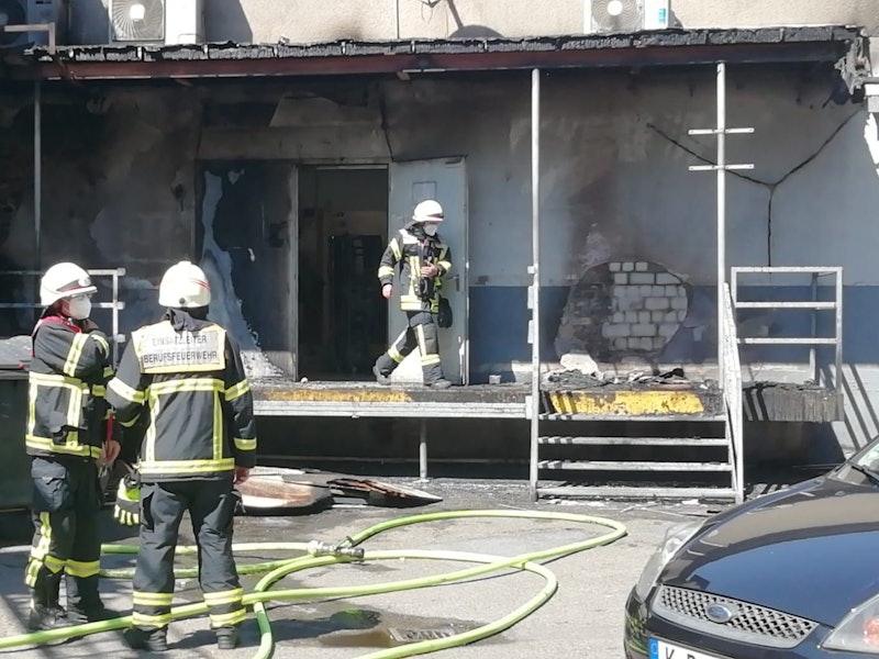 Ein Feuerwehrmann kommt aus einem Gebäude, in dem es gebrannt hat, zwei Kollegen stehen davor, zu ihren Füßen Löschschläuche.