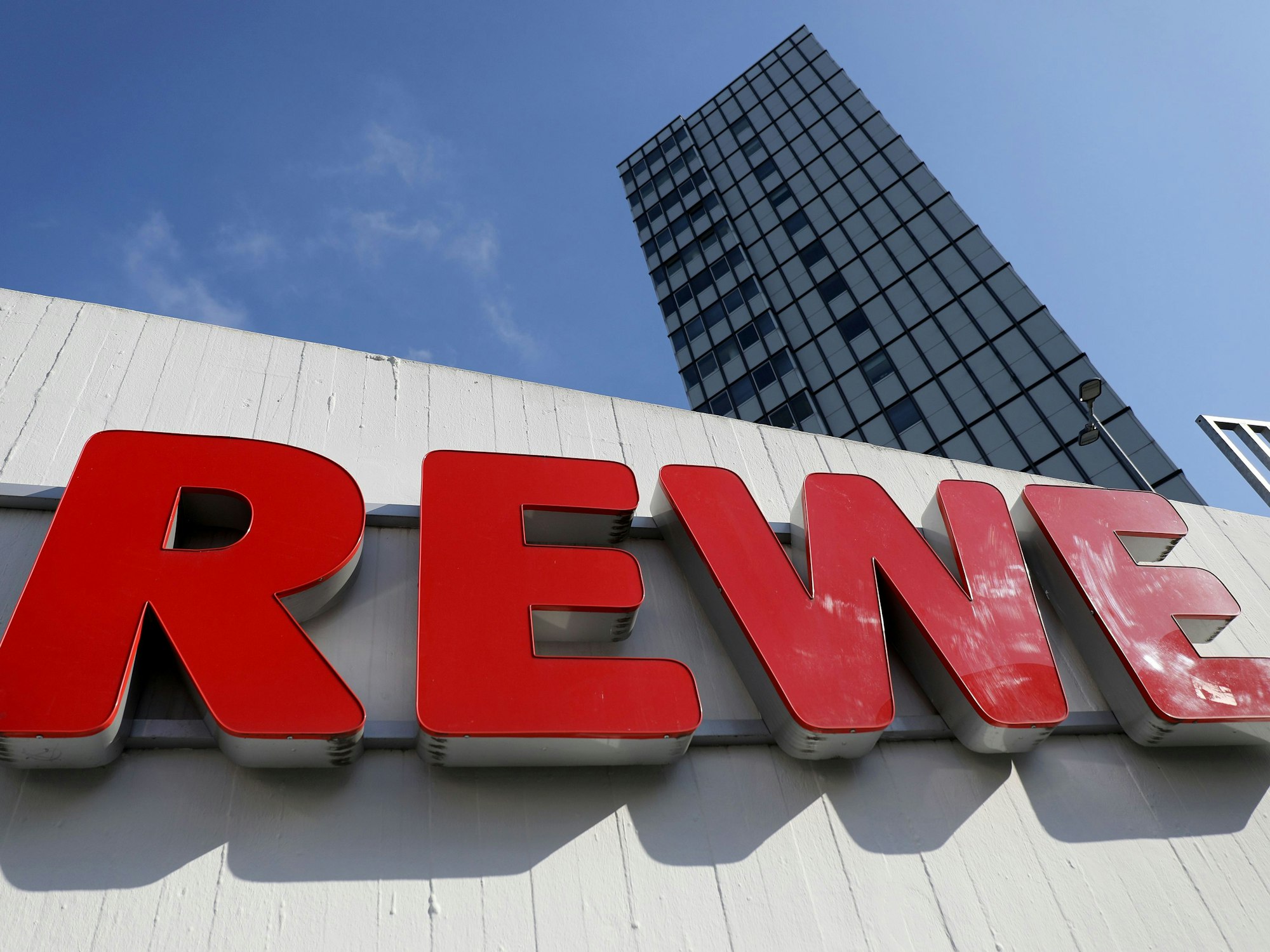 Ein Rewe-Schriftzug hängt vor einem Supermarkt.