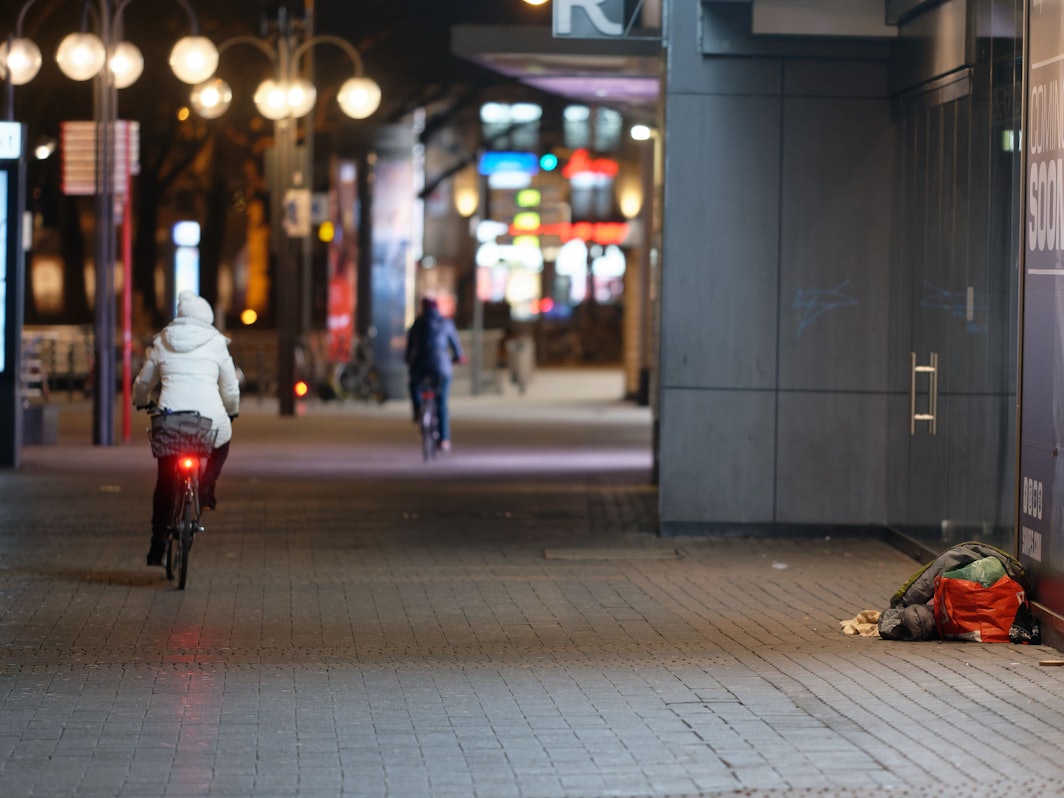 Ein Mensch liegt in der Innenstadt in einem Schlafsack im Eingang zu einem Geschäft. Die FDP will einen Antrag für ein Pilotprojekt für Köln stellen – eine Alarmanlage für Obdachlose soll her.