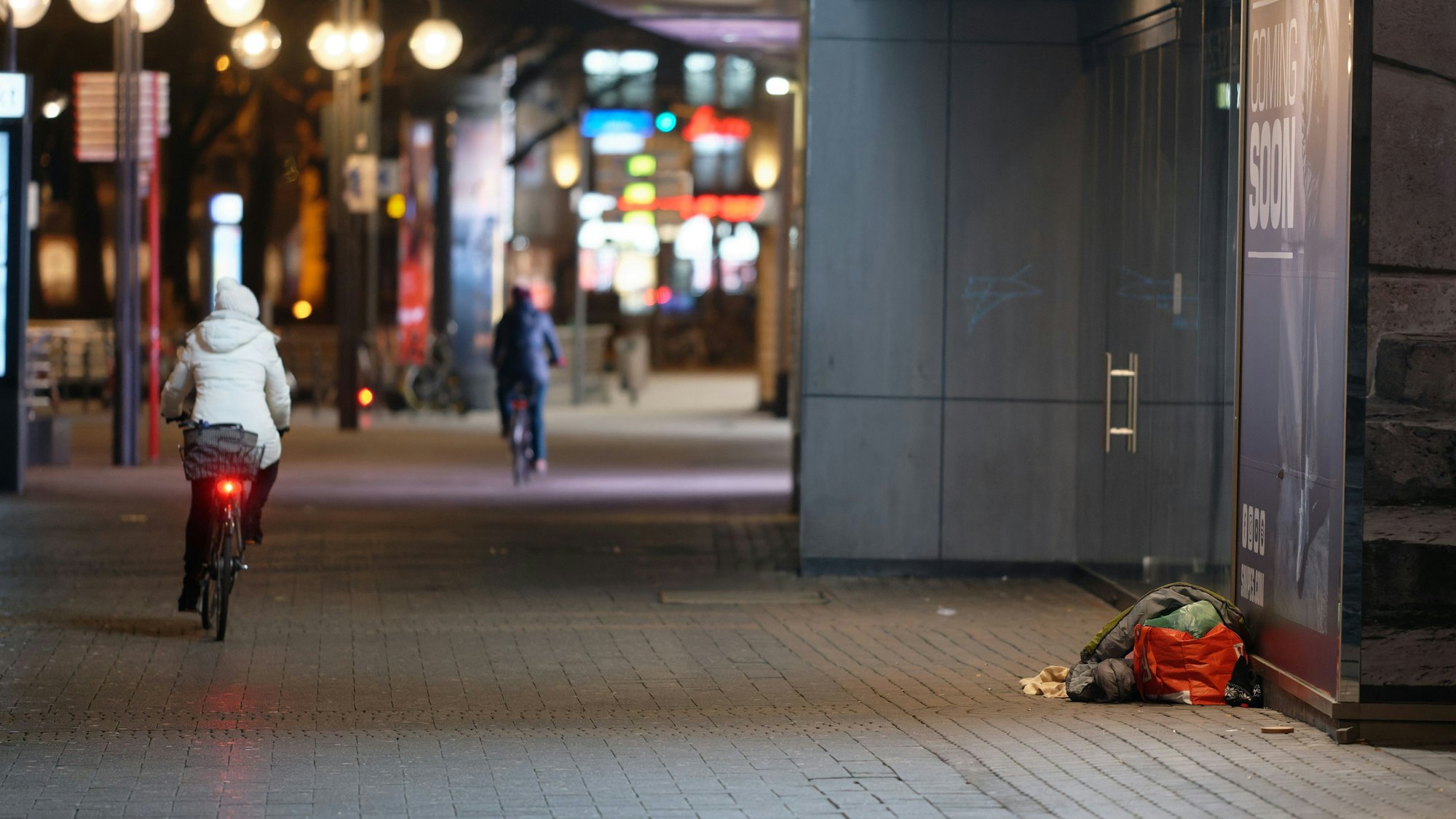 Ein Mensch liegt in der Innenstadt in einem Schlafsack im Eingang zu einem Geschäft. Die FDP will einen Antrag für ein Pilotprojekt für Köln stellen – eine Alarmanlage für Obdachlose soll her.