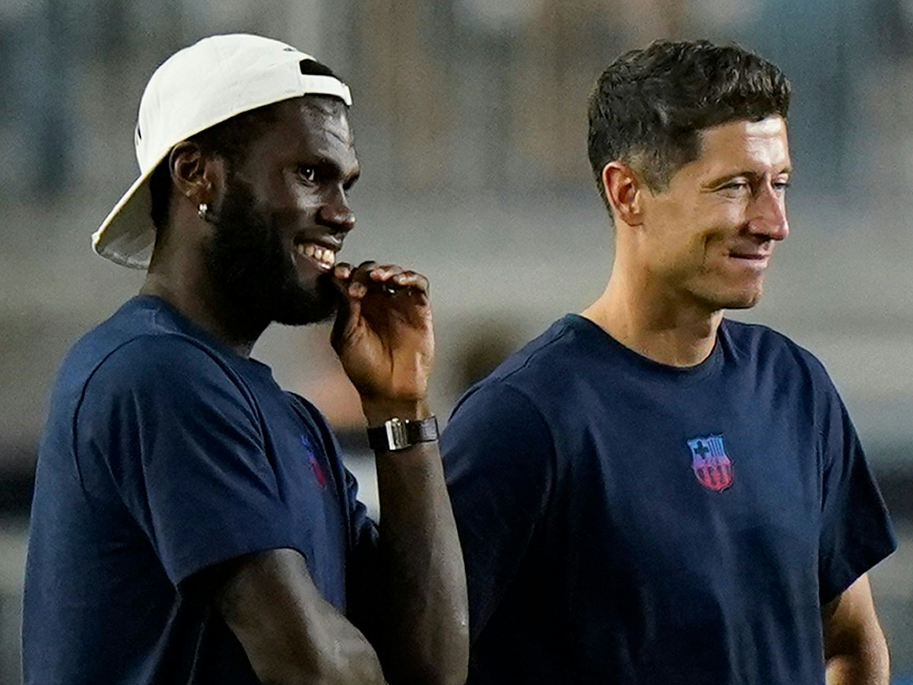 Robert Lewandowski steht im T-Shirt des FC Barcelona neben Franck Kessie, der eine Kappe trägt.