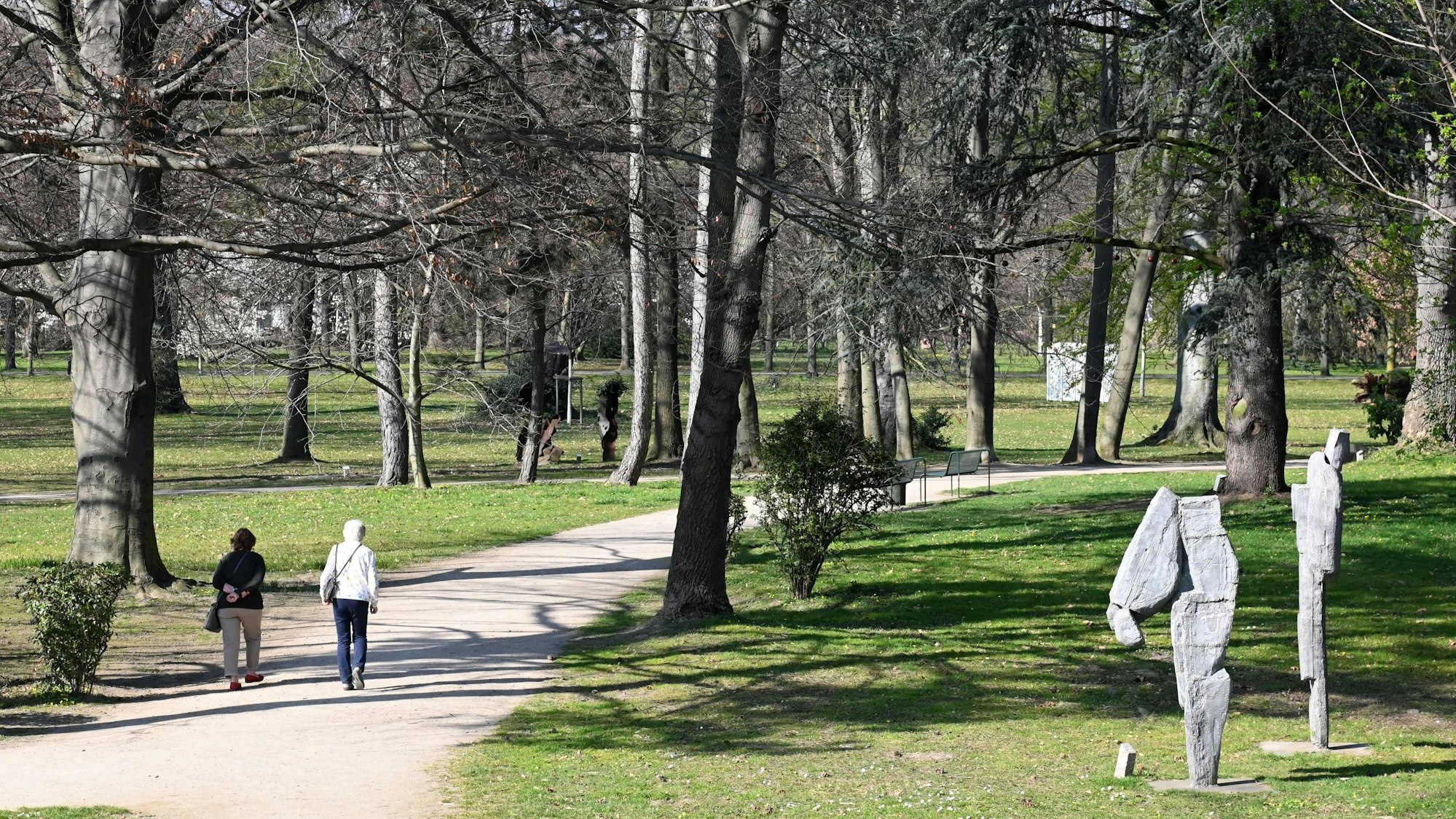 Skulpturen stehen und Fußgänger gehen am 24. März 2022 im Schlosspark in Köln-Stammheim spazieren.