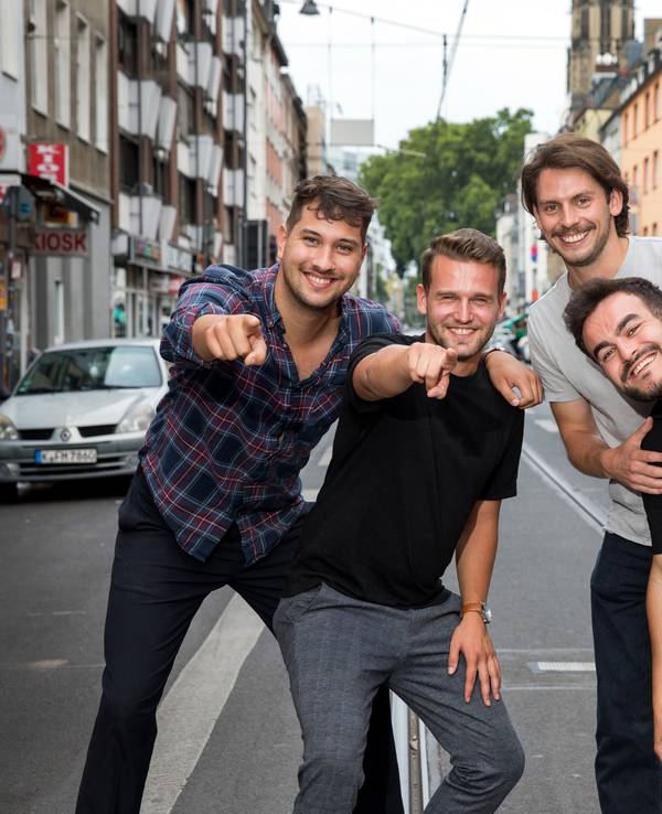 Vier Studenten stehen auf der Zülpicher Straße und deuten in die Kamera. Sie alle sind Teil von Malle Anja, die Band hat jetzt einen Mallorca-Hit.
