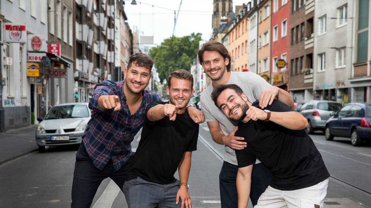 Vier Studenten stehen auf der Zülpicher Straße und deuten in die Kamera. Sie alle sind Teil von Malle Anja, die Band hat jetzt einen Mallorca-Hit.