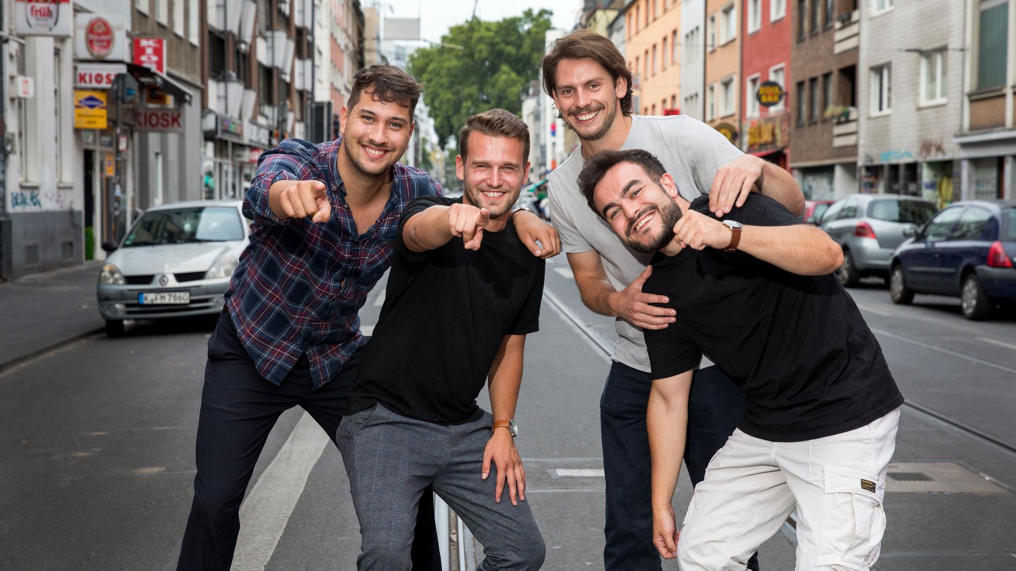 Vier Studenten stehen auf der Zülpicher Straße und deuten in die Kamera. Sie alle sind Teil von Malle Anja, die Band hat jetzt einen Mallorca-Hit.