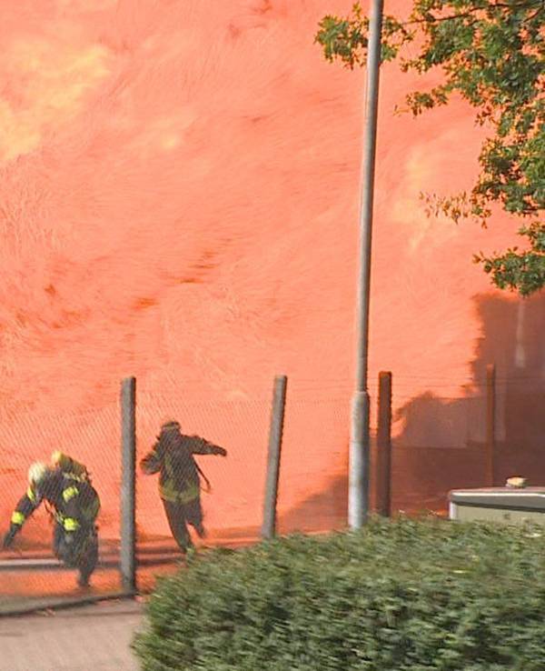 Feuerwehrleute rennen vor einer Flammenwand weg.