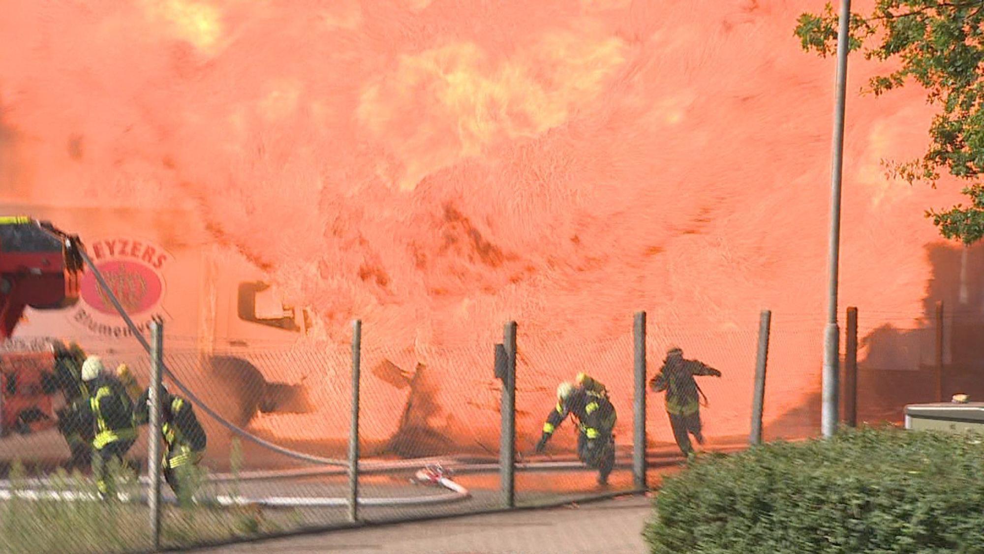 Feuerwehrleute rennen vor einer Flammenwand weg.