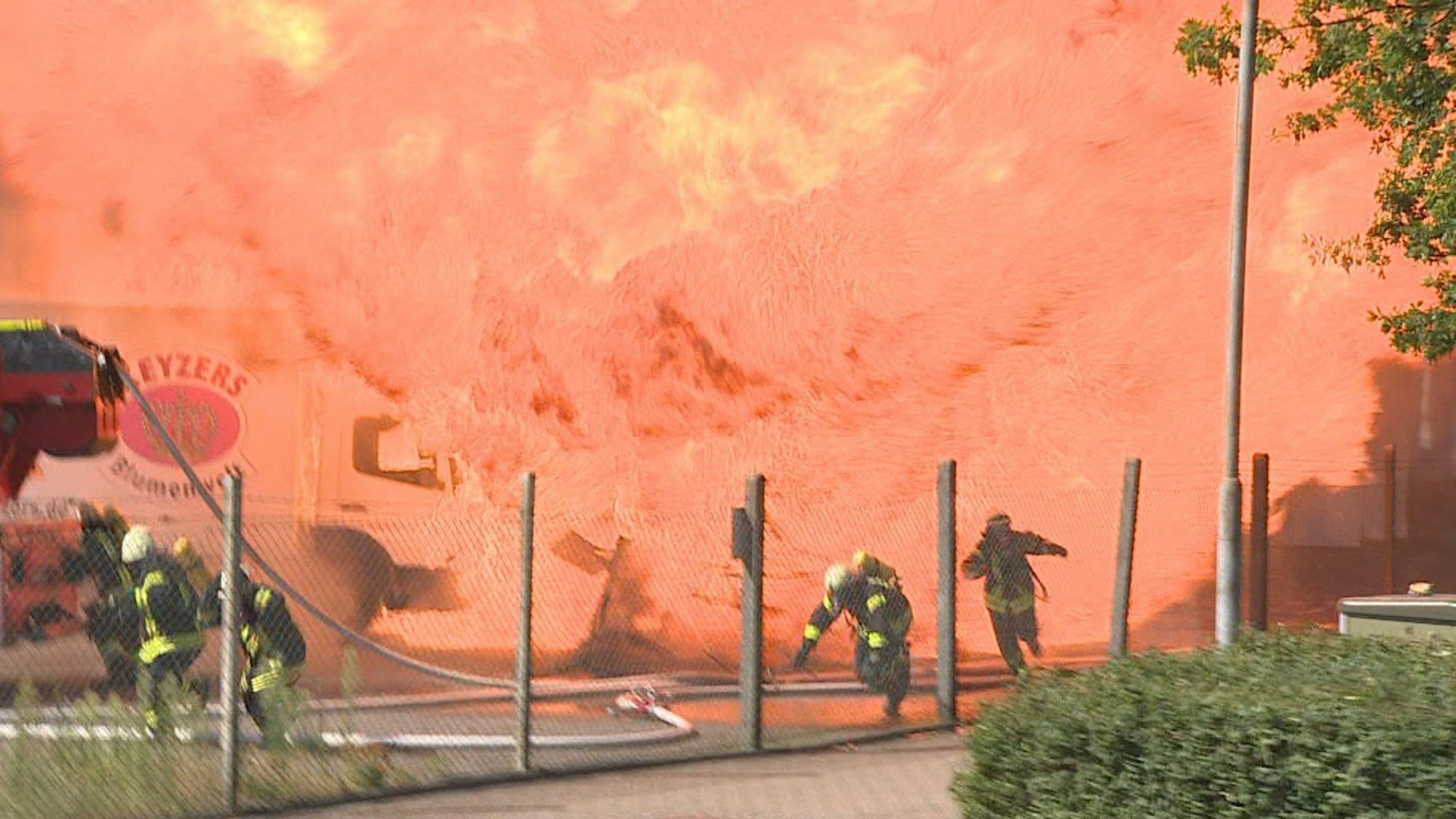 Feuerwehrleute rennen vor einer Flammenwand weg.