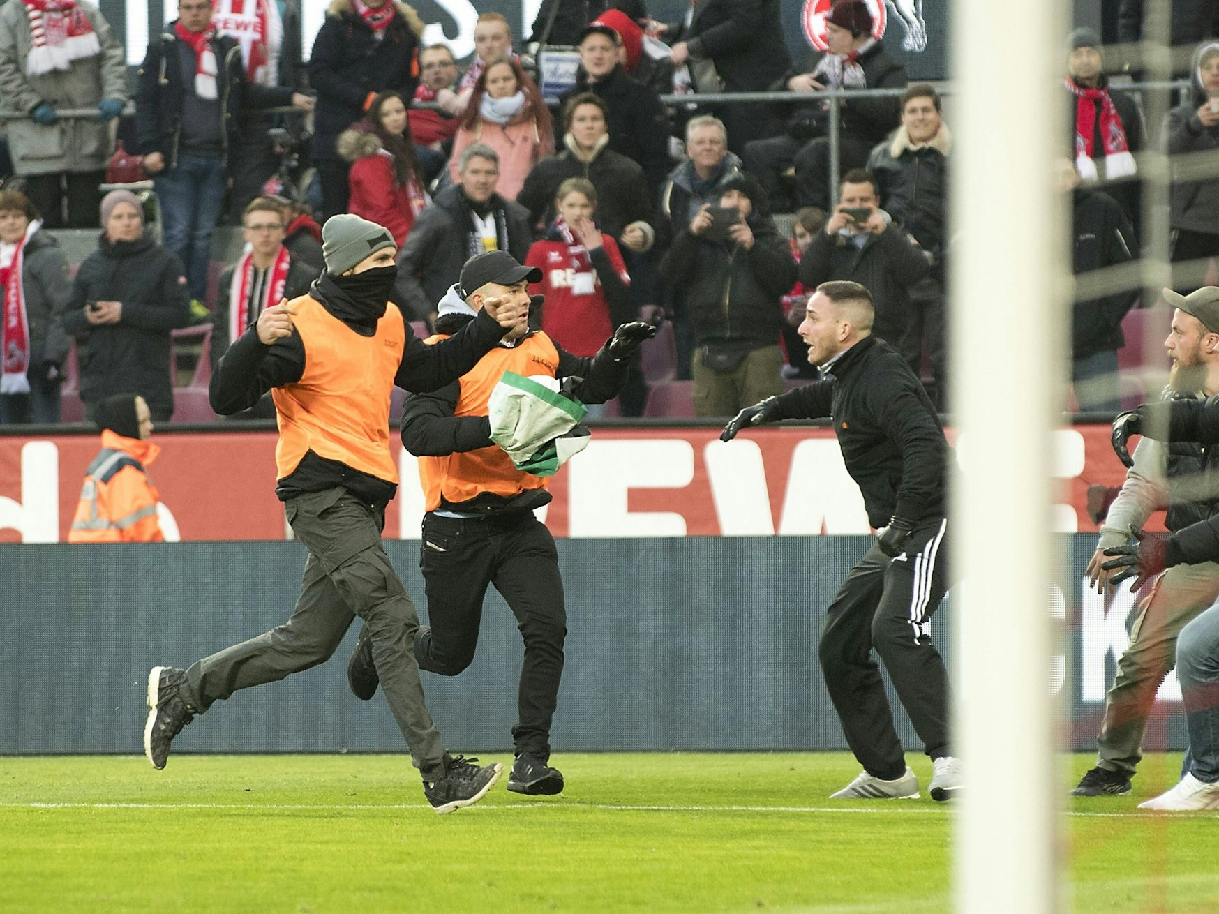 Ordner klauen eine Fahne der MG Fans und rennen damit über den Platz zu den Kölner Fans.