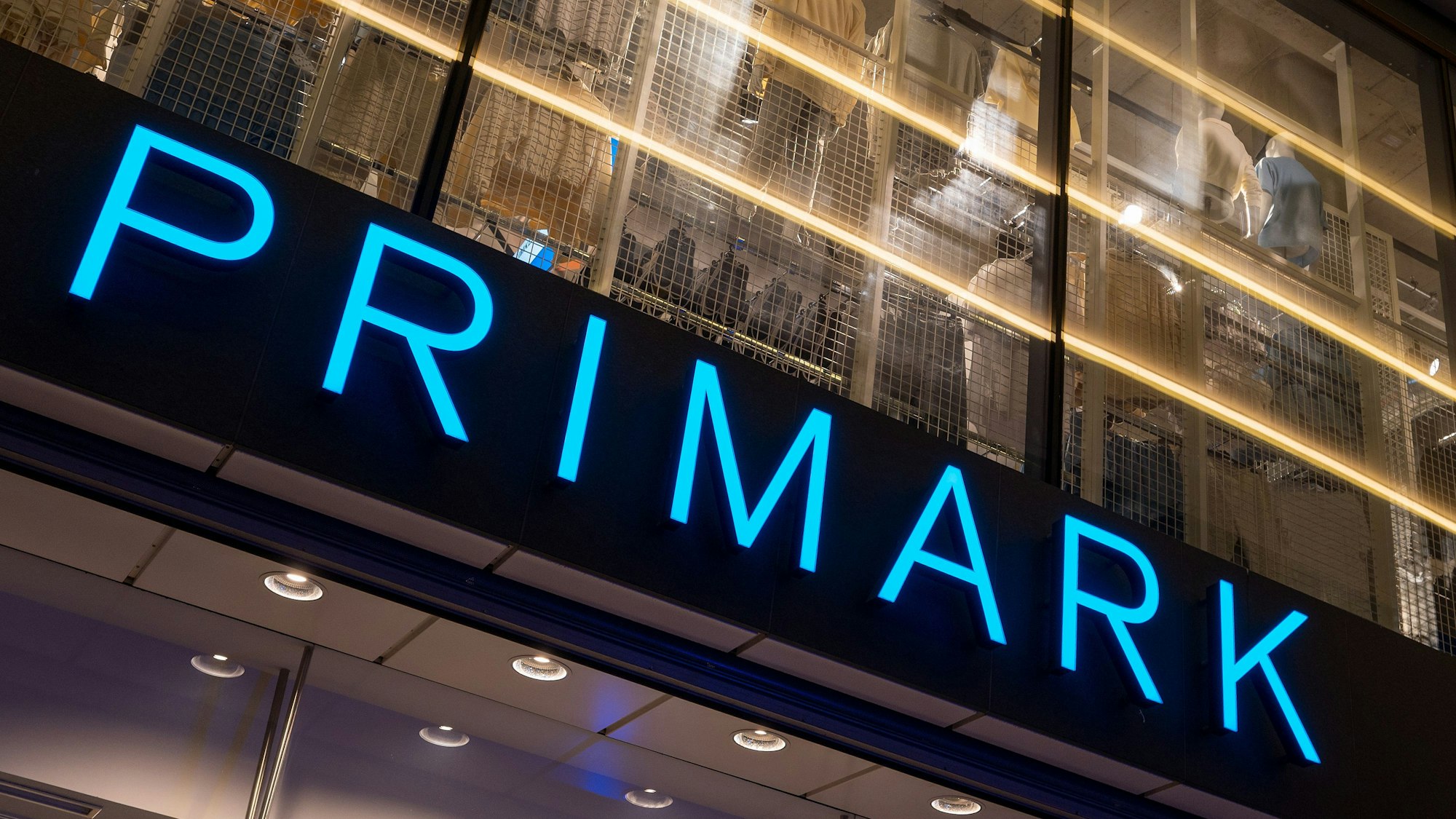 Das Logo des Bekleidungsgeschäfts Primark leuchtet am Abend an der Fassade.
