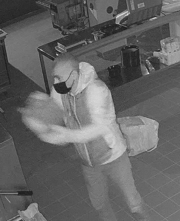 Mann steht in einer Pizzeria und verschüttet eine Flüssigkeit. Nach ihm wird nun öffentlich gefahndet.