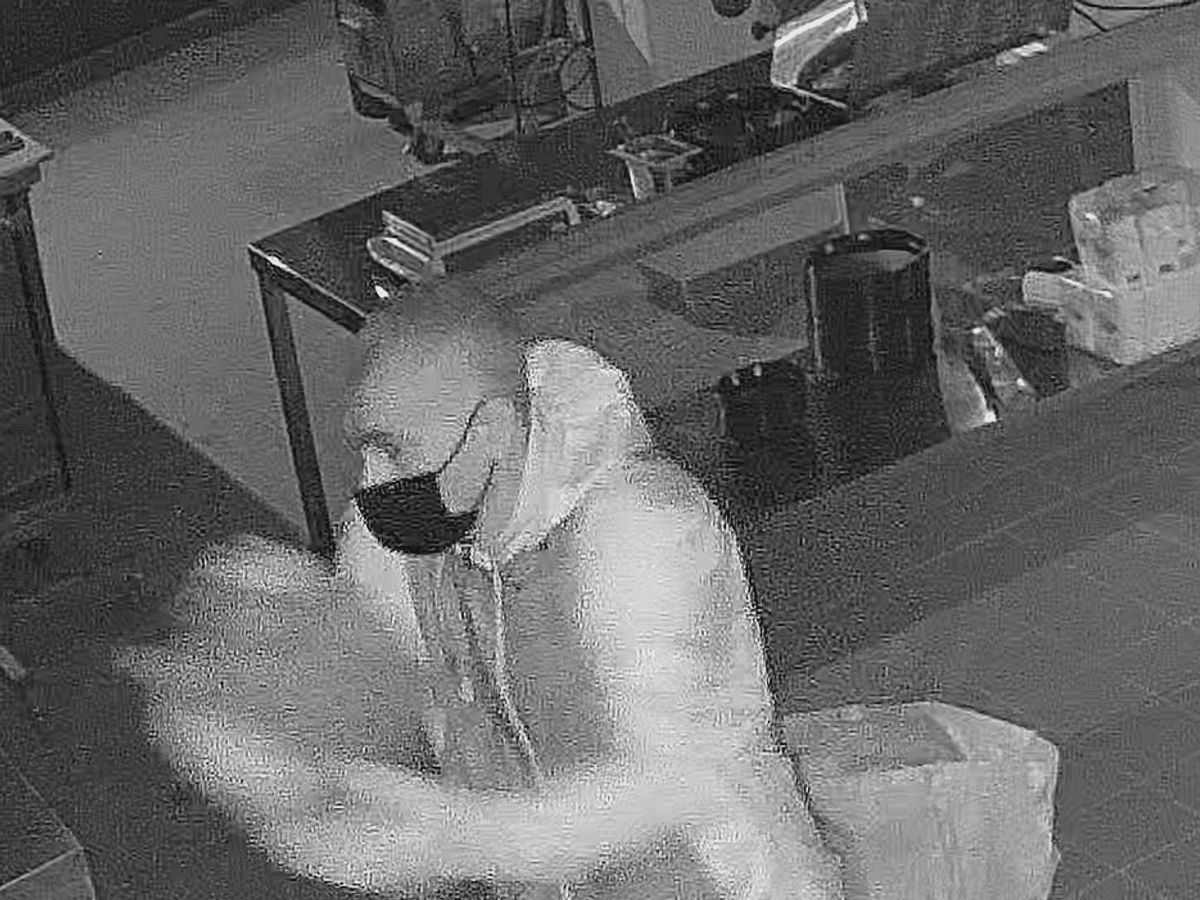 Mann steht in einer Pizzeria und verschüttet eine Flüssigkeit. Nach ihm wird nun öffentlich gefahndet.