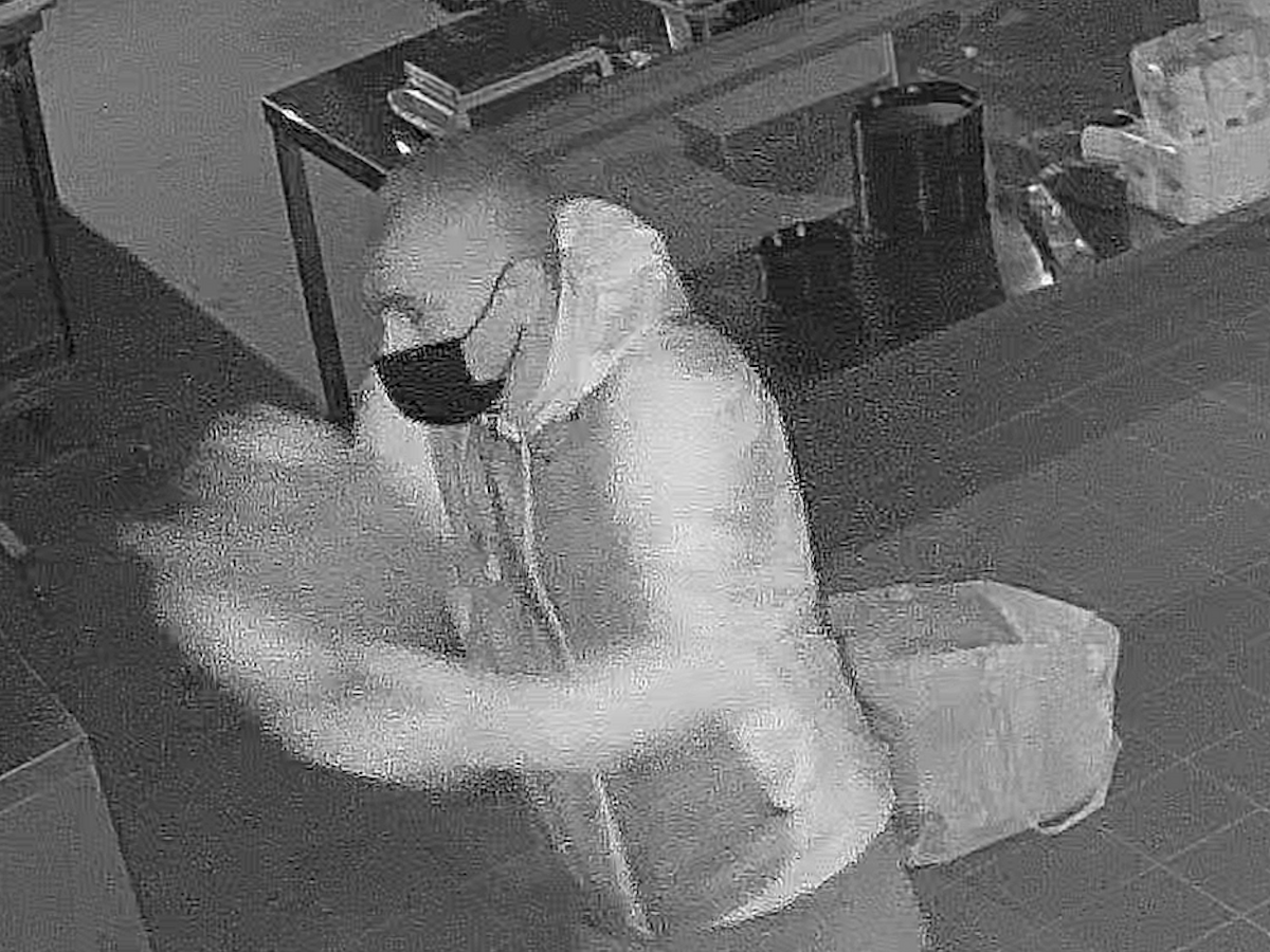 Mann steht in einer Pizzeria und verschüttet eine Flüssigkeit. Nach ihm wird nun öffentlich gefahndet.