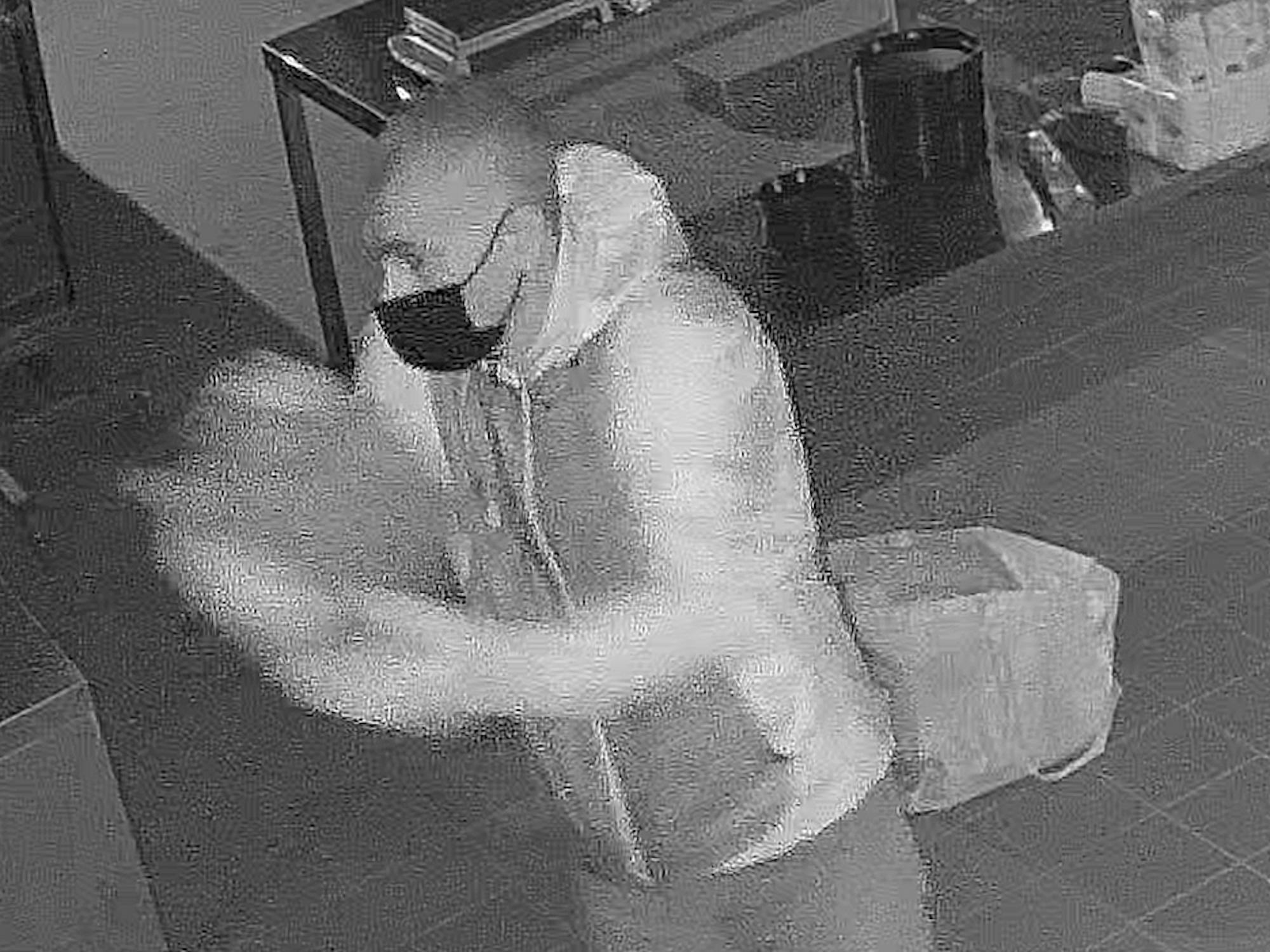 Mann steht in einer Pizzeria und verschüttet eine Flüssigkeit. Nach ihm wird nun öffentlich gefahndet.