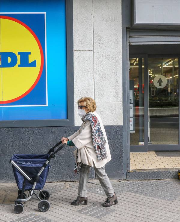 Eine Frau mit Rollator trägt einen Mund-Nasen-Schutz und passiert ein Einkaufsladen von Lidl.