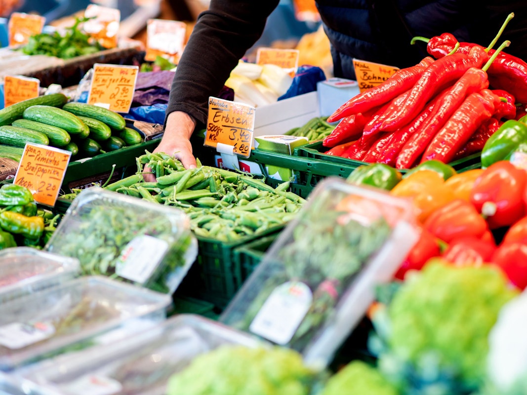 Ein Verkäufer greift an einem Obst- und Gemüsestand auf dem Wochenmarkt in Oldenburg im August 2022 in eine Kiste mit Erbsen.
