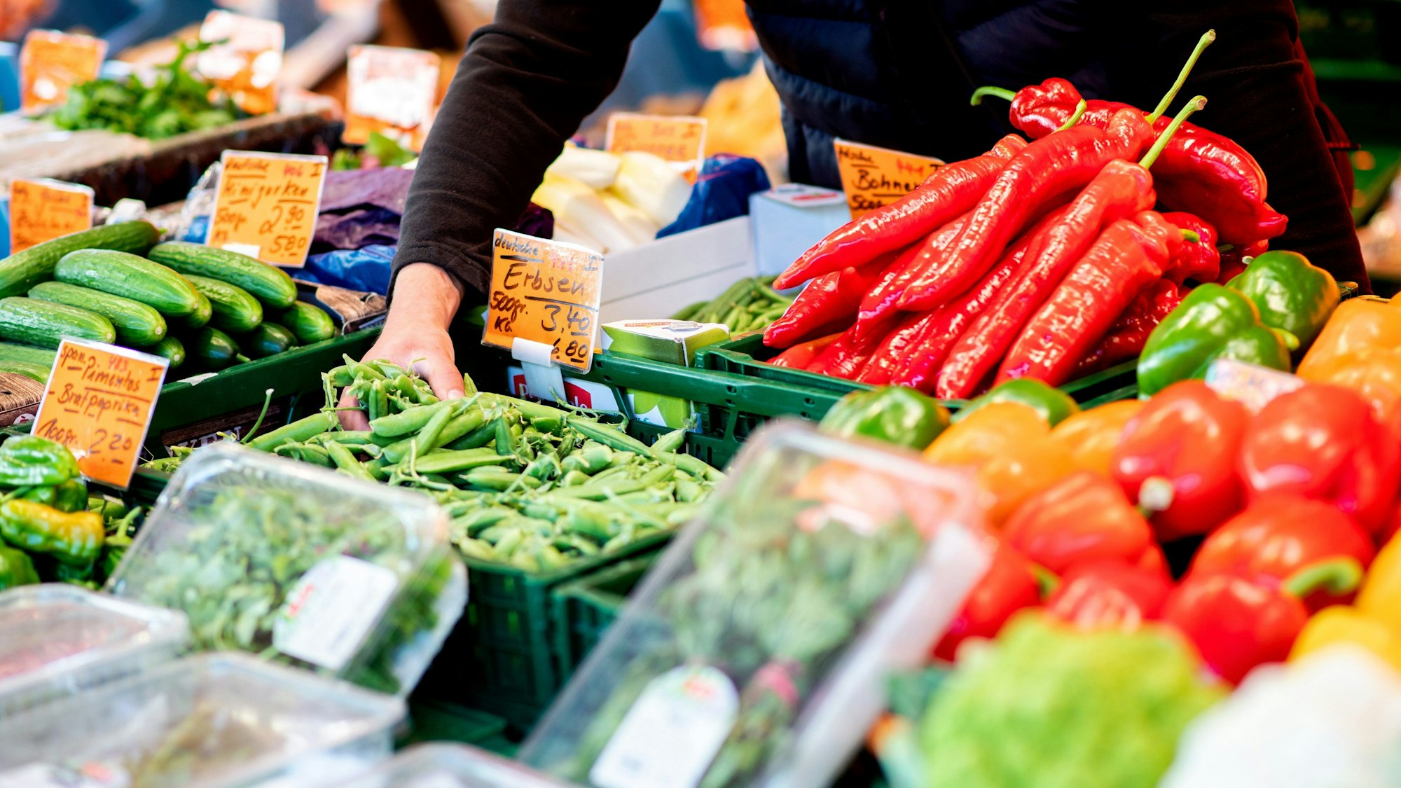Ein Verkäufer greift an einem Obst- und Gemüsestand auf dem Wochenmarkt in Oldenburg im August 2022 in eine Kiste mit Erbsen.
