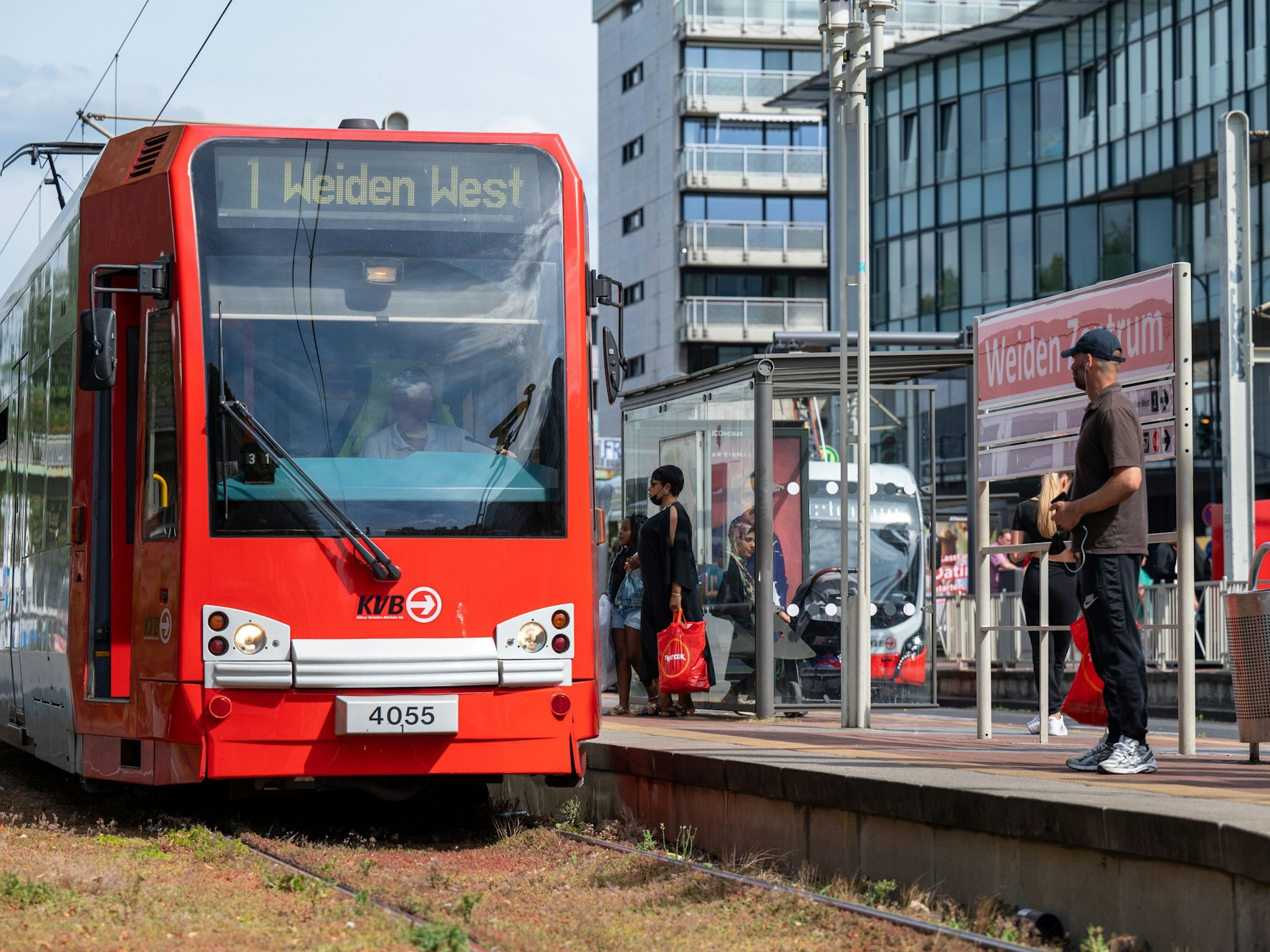 Menschen warten auf die KVB-Linie 1 an der Haltestelle Weiden Zentrum.