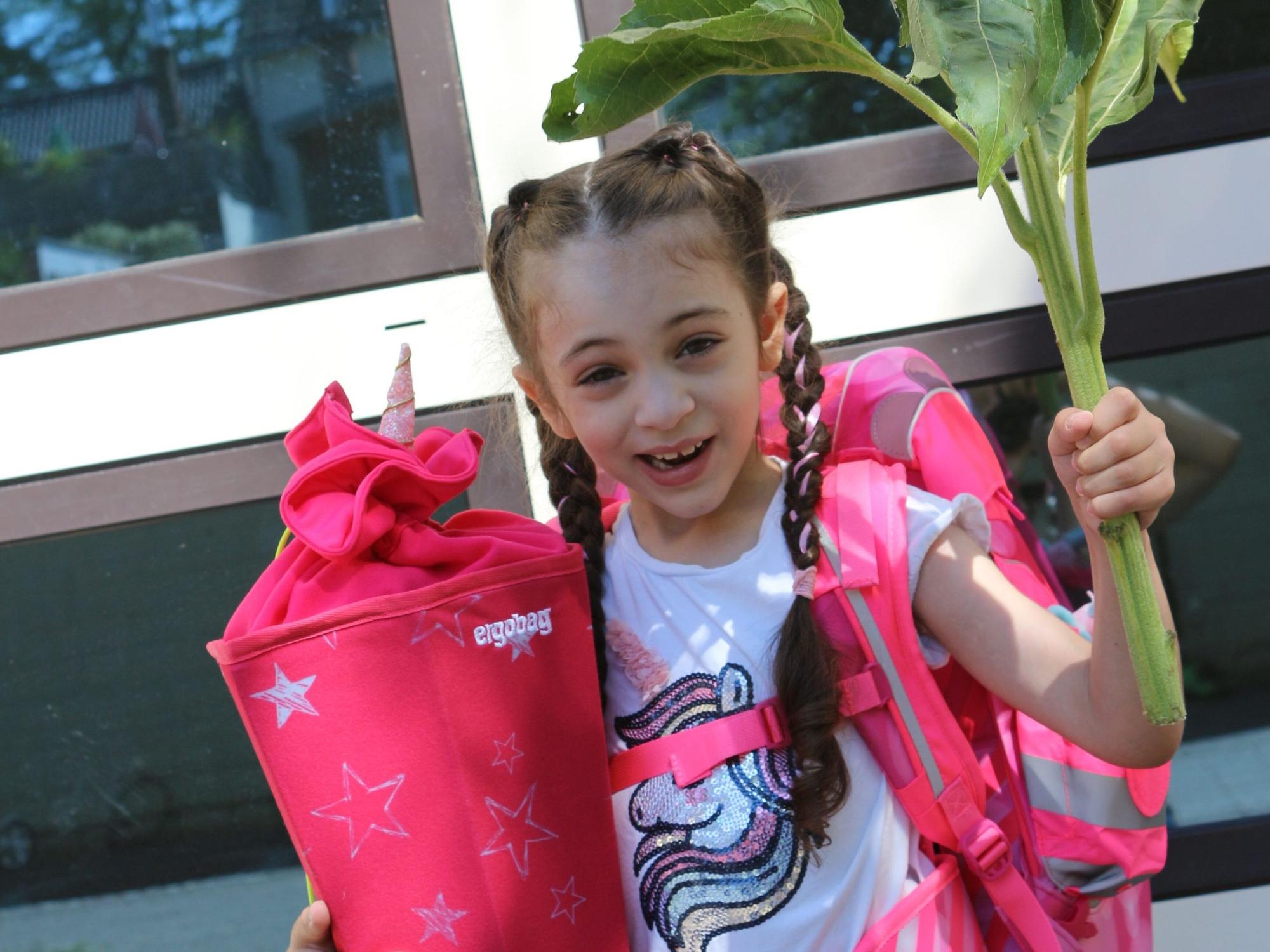 Kleines Mädchen steht mit Blume und Schultüte bei ihrer Einschulung.