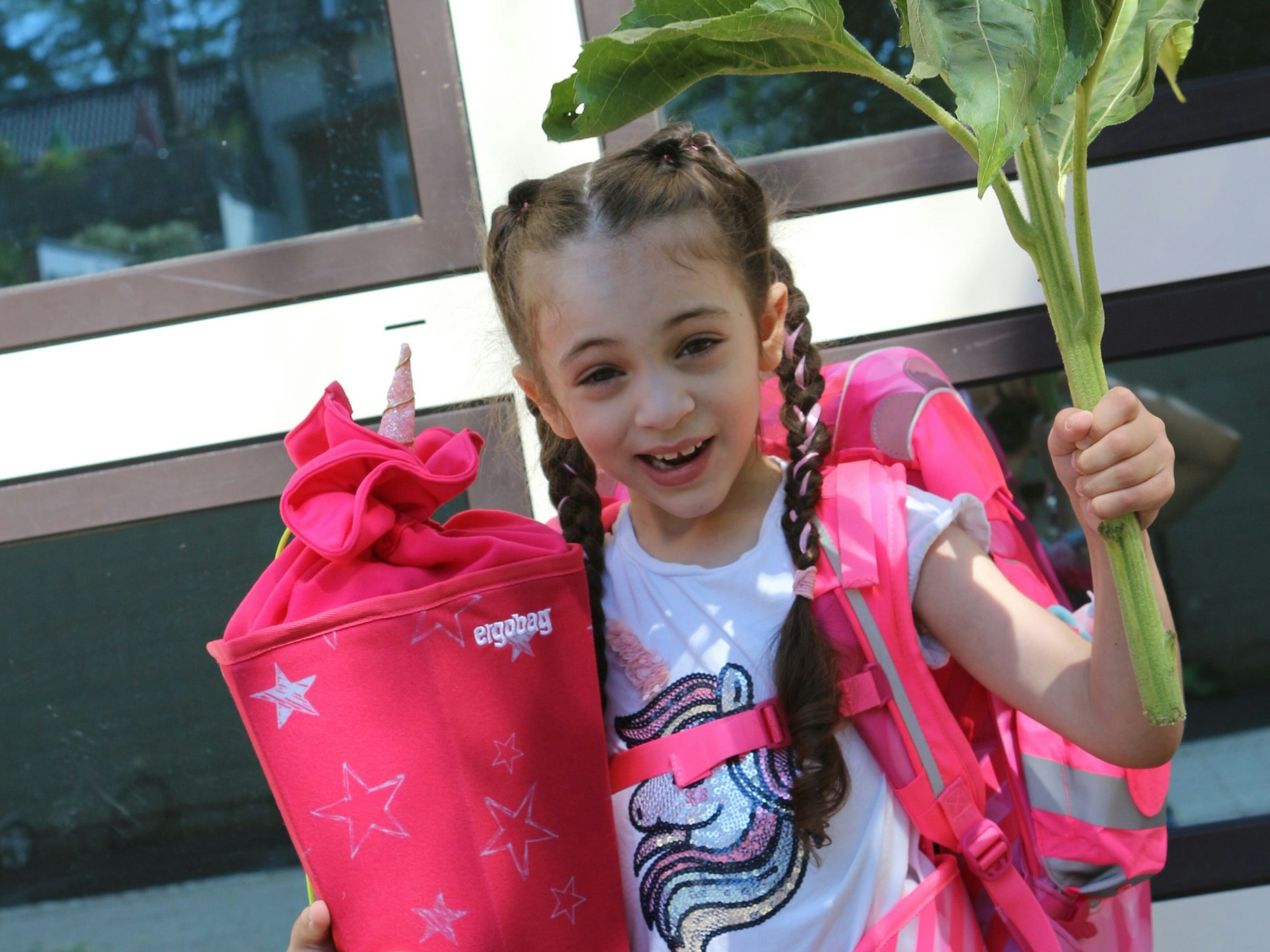 Kleines Mädchen steht mit Blume und Schultüte bei ihrer Einschulung.