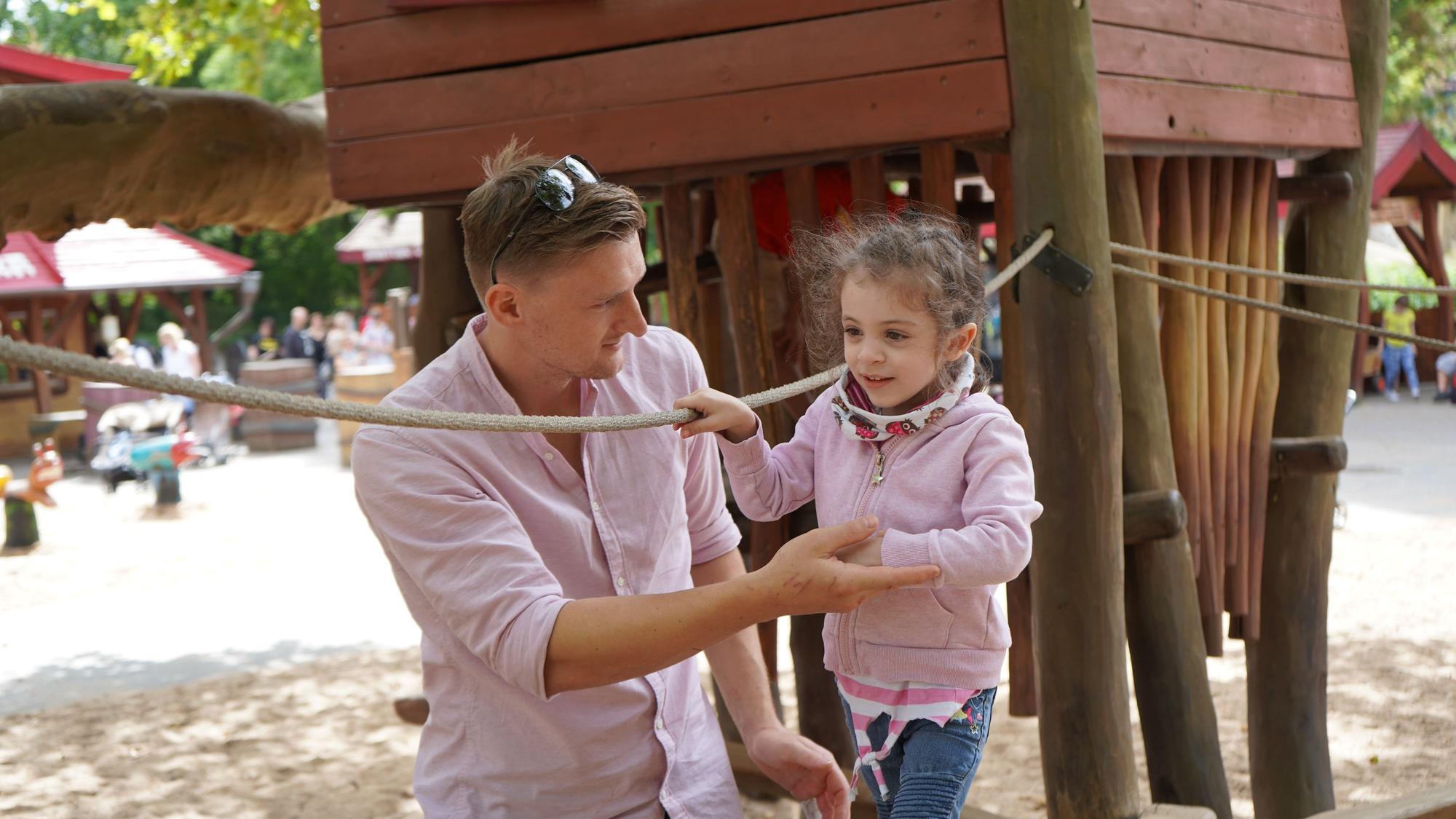 Das kleine Mädchen Sofia klettert im Kölner Zoo über ein Gerät, ihr Spender Ben Zimdahl hilft ihr.