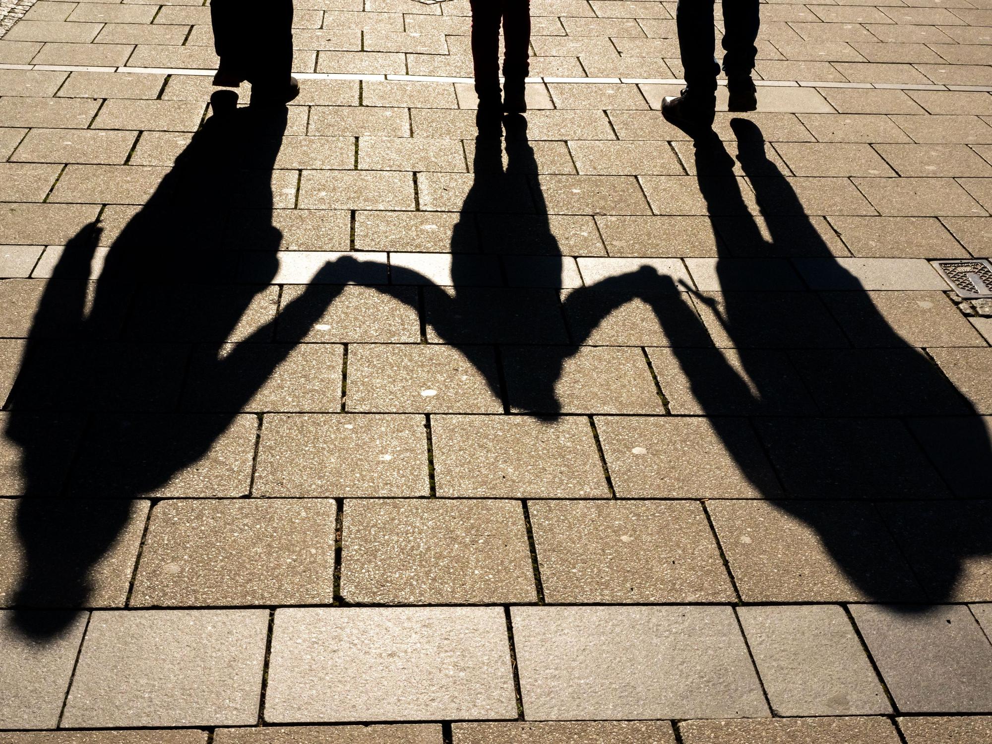 Die Schatten von zwei Erwachsenen und einem Kind sind in den Morgenstunden auf dem Asphalt in der Innenstadt zu sehen.