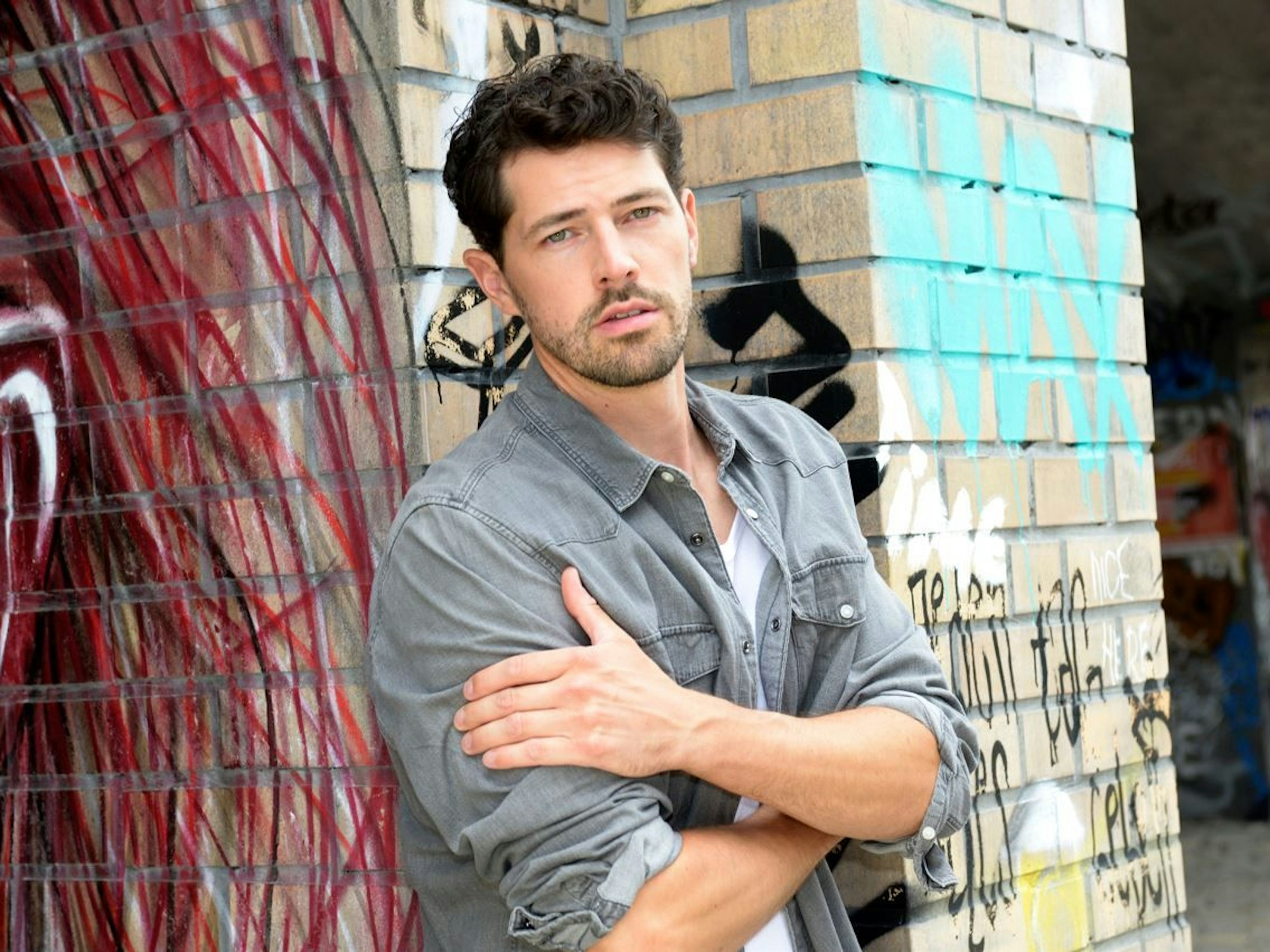 Daniel Noah aus Köln lehnt an einer Mauer und schaut beim Fotoshooting in die Kamera.