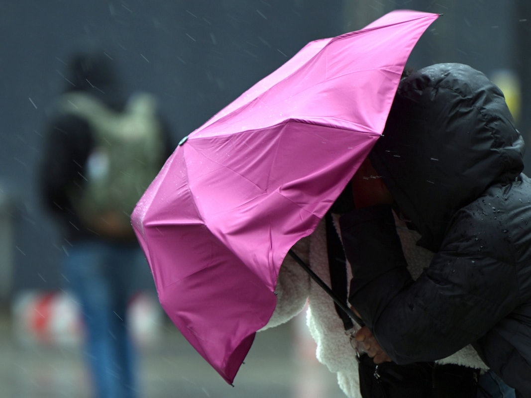 Eine Passantin in Köln kämpft bei Regen und Sturm mit ihrem Regenschirm. Symbolaufnahme von Februar 2022.