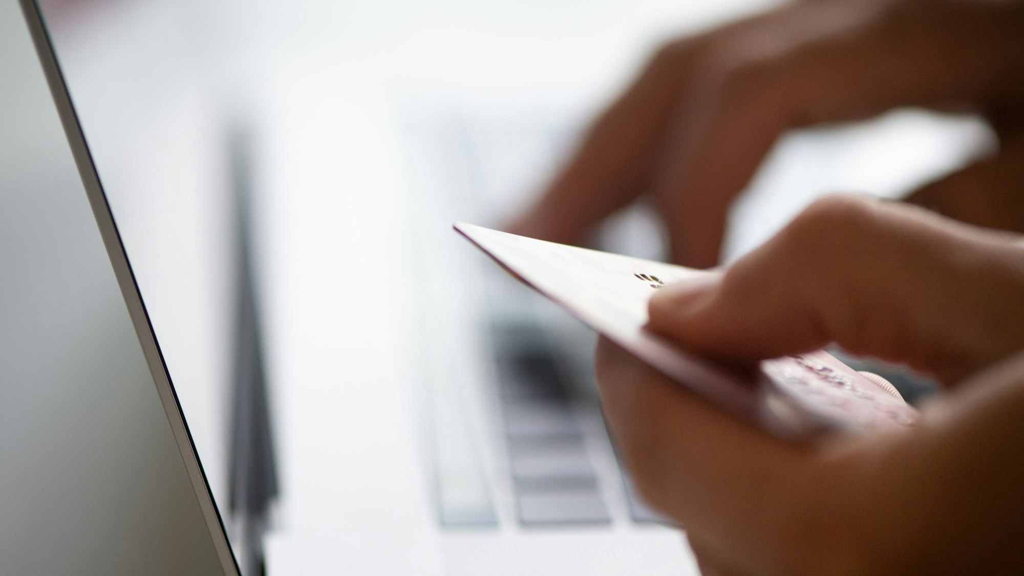 Das Foto zeigt eine Frau, die an einem Laptop sitzt und ihre Kreditkarte in der Hand hält (Symbolfoto)