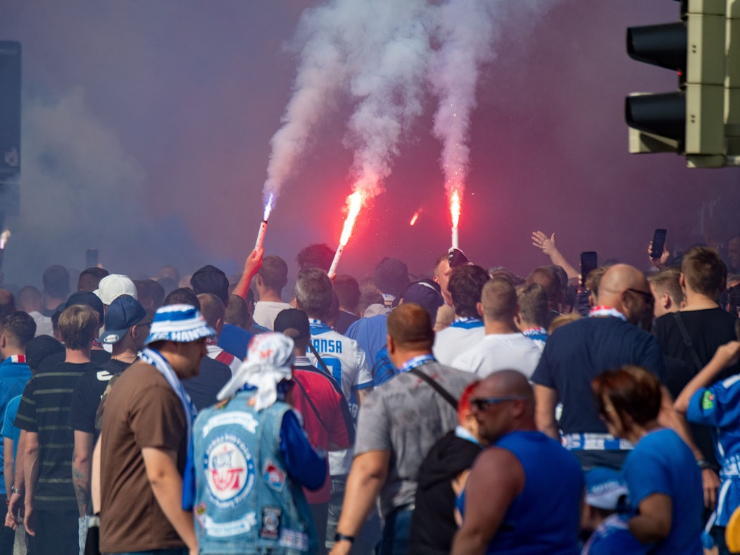 Fußballfans von Hansa Rostock laufen mit bengalischen Fackeln durch die Stadt.
