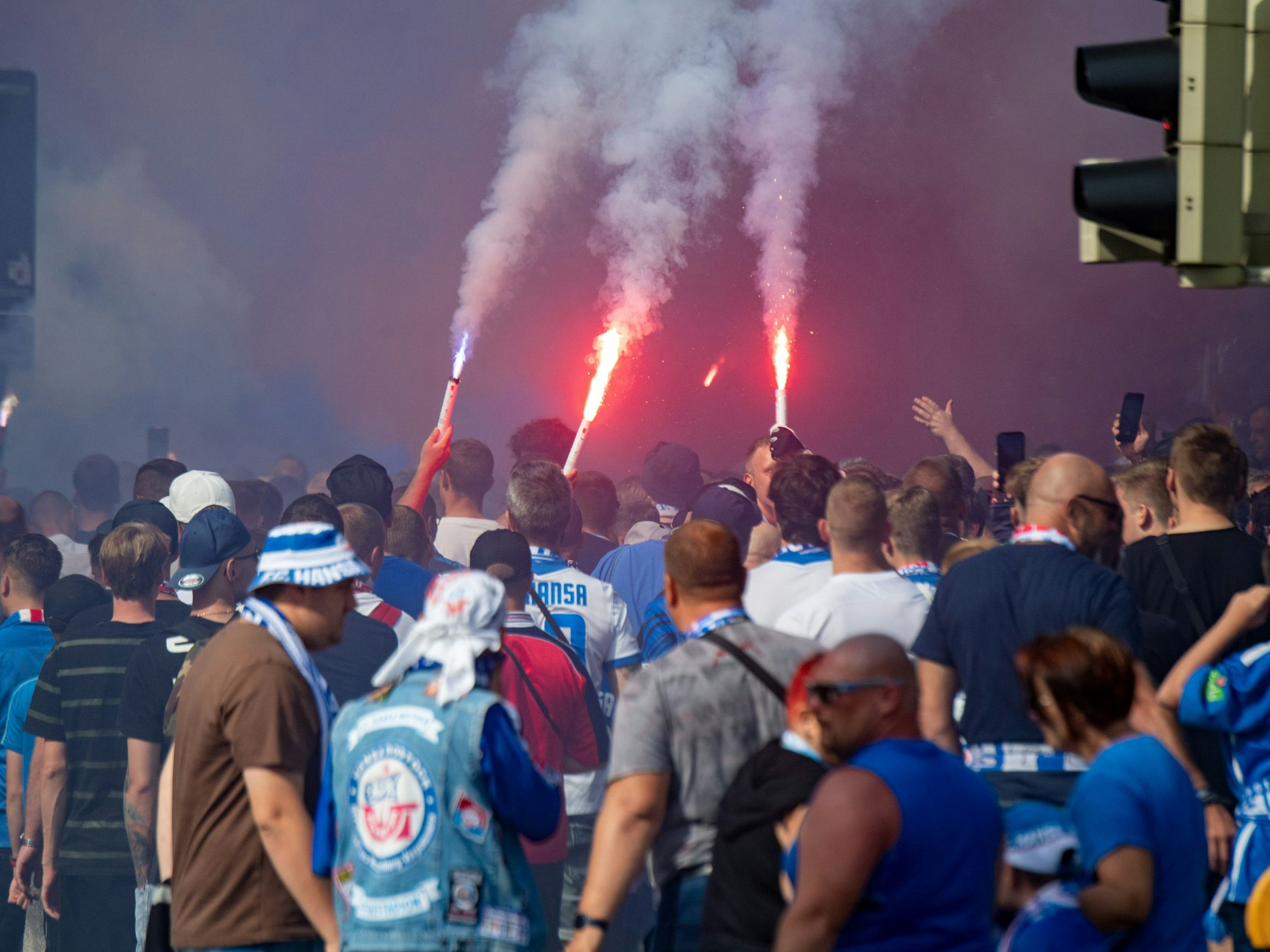 Fußballfans von Hansa Rostock laufen mit bengalischen Fackeln durch die Stadt.