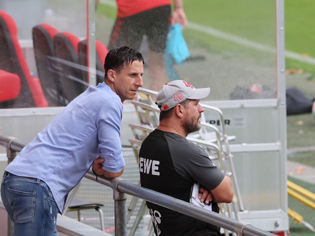 FC-Sportchef Christian Keller (l.) lehnt sich hinter Trainer Steffen Baumgart ans Geländer am Geißbockheim.