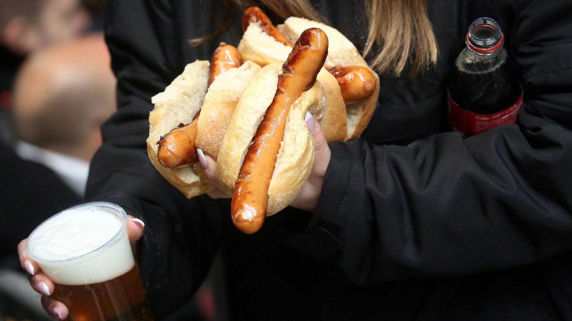 Eine Frau trägt im Stadion Bratwürste im Brötchen und Bier zu ihrem Platz.