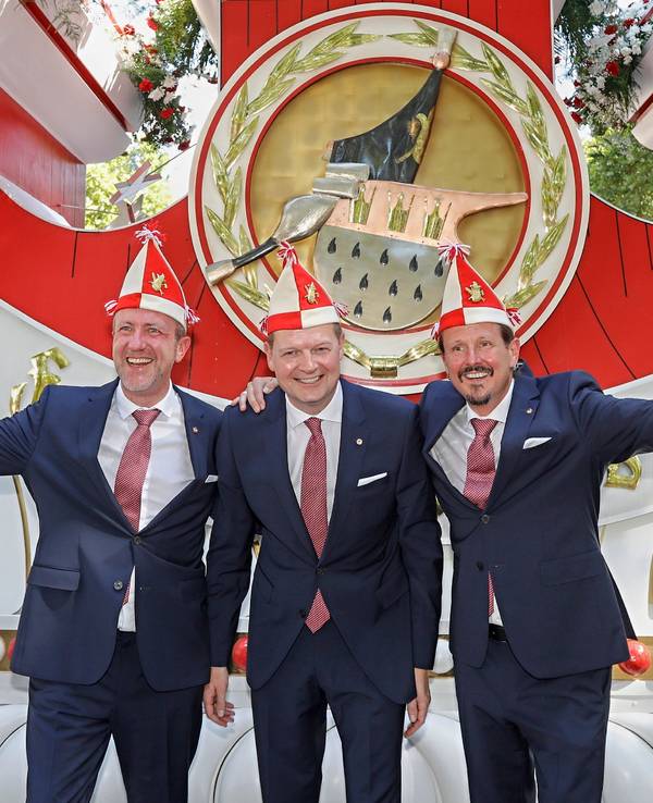 Prinz, Bauer und Jungfrau des neuen Kölner Dreigestirns stehen vor einem Wagen der Roten Funken.
