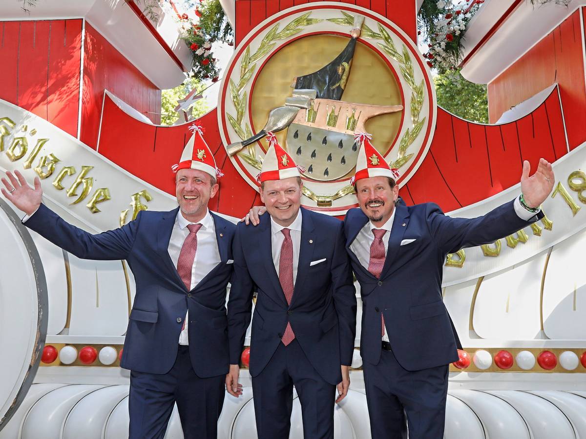 Prinz, Bauer und Jungfrau des neuen Kölner Dreigestirns stehen vor einem Wagen der Roten Funken.