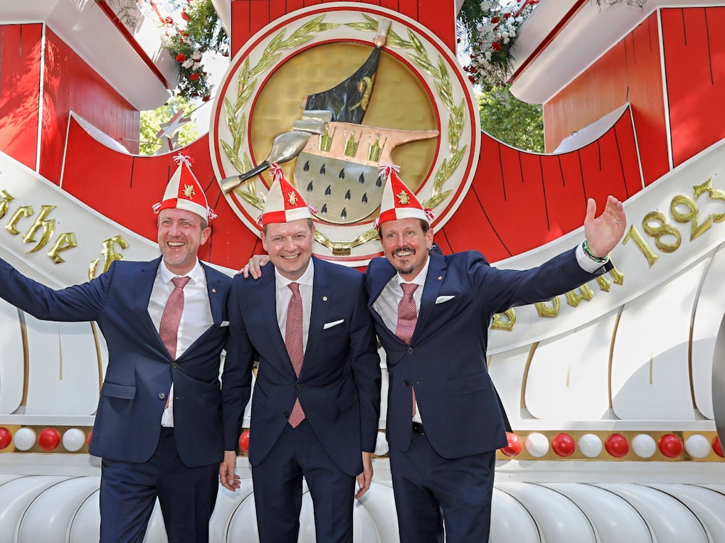 Prinz, Bauer und Jungfrau des neuen Kölner Dreigestirns stehen vor einem Wagen der Roten Funken.