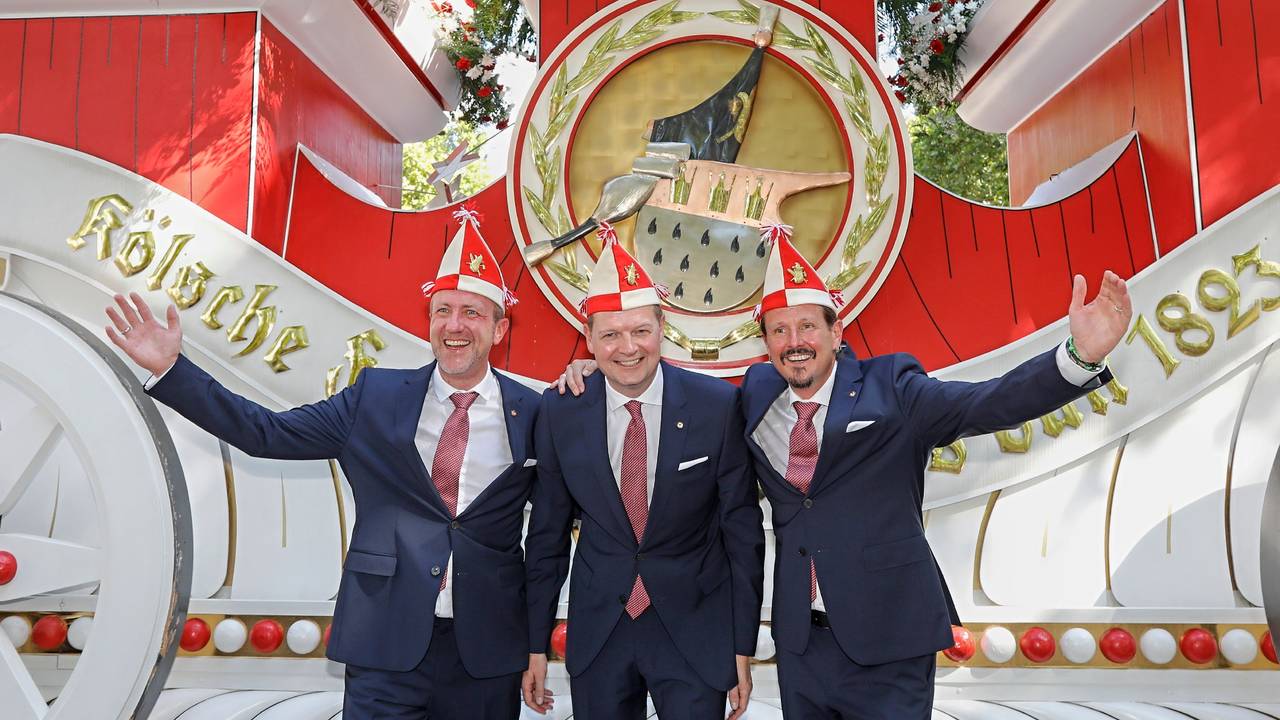 Prinz, Bauer und Jungfrau des neuen Kölner Dreigestirns stehen vor einem Wagen der Roten Funken.