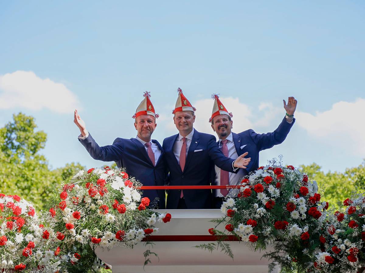 Das Kölner Dreigestirn winkt von einem Wagen der Roten Funken.
