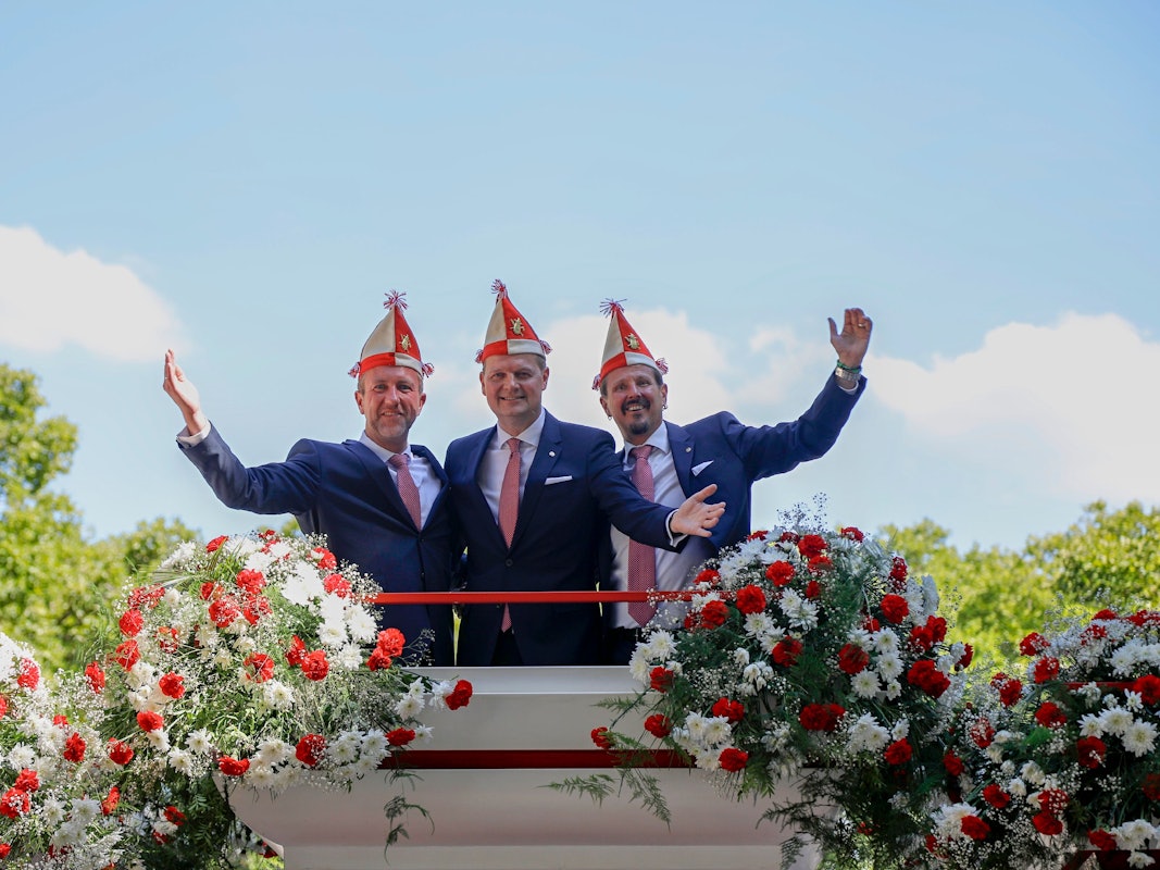 Das Kölner Dreigestirn winkt von einem Wagen der Roten Funken.