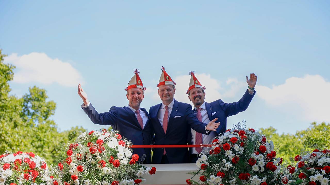 Das Kölner Dreigestirn winkt von einem Wagen der Roten Funken.