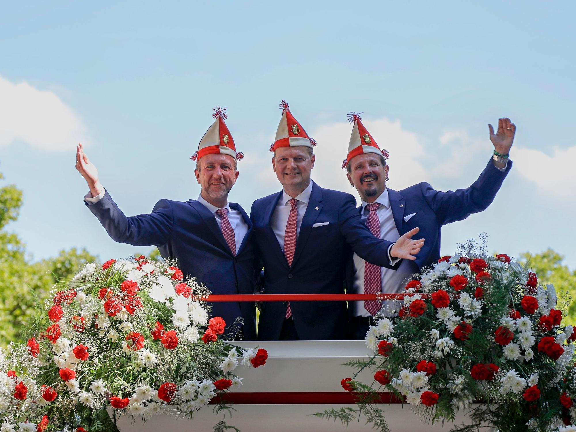 Das Kölner Dreigestirn winkt von einem Wagen der Roten Funken.