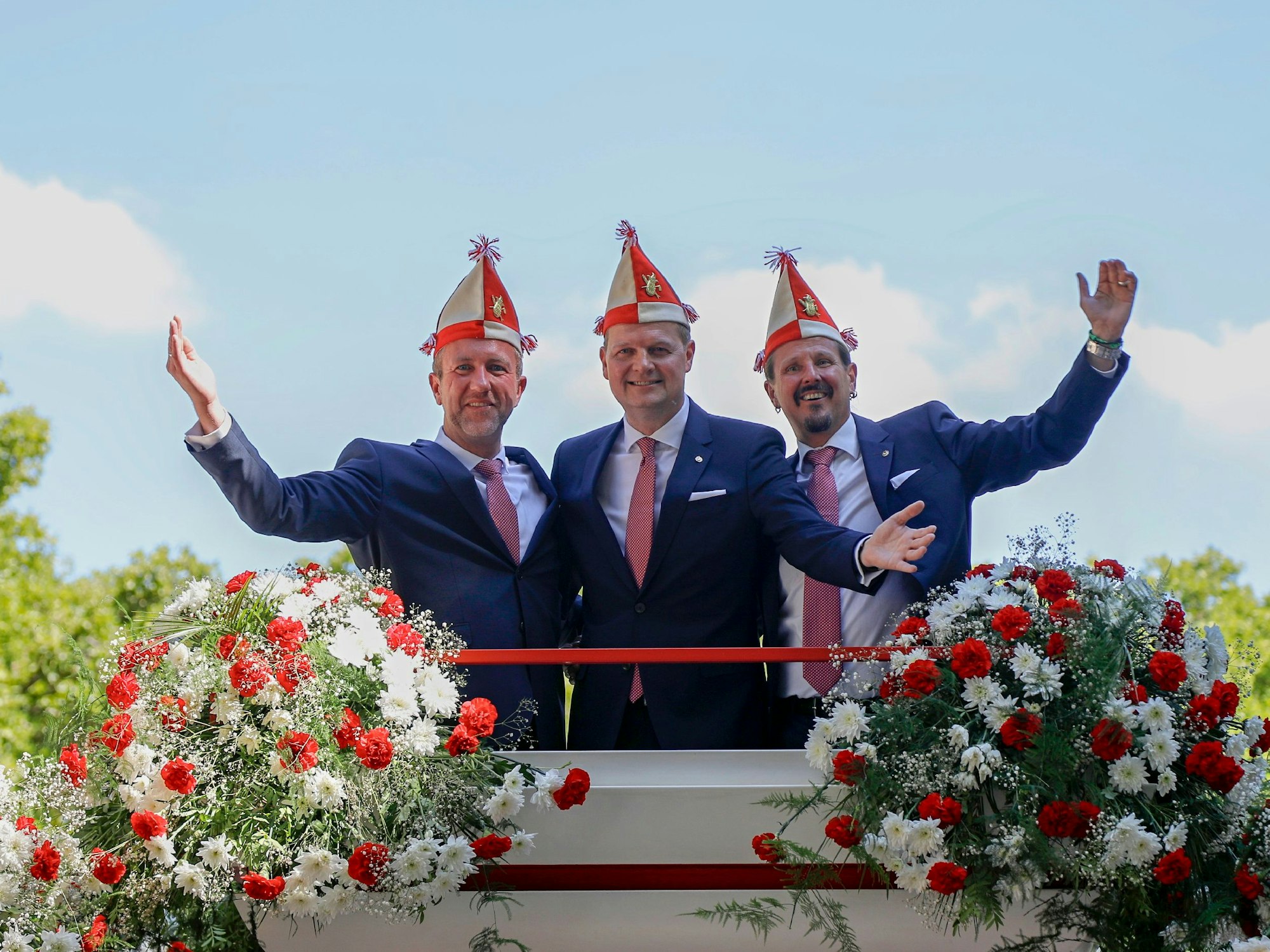 Das Kölner Dreigestirn winkt von einem Wagen der Roten Funken.