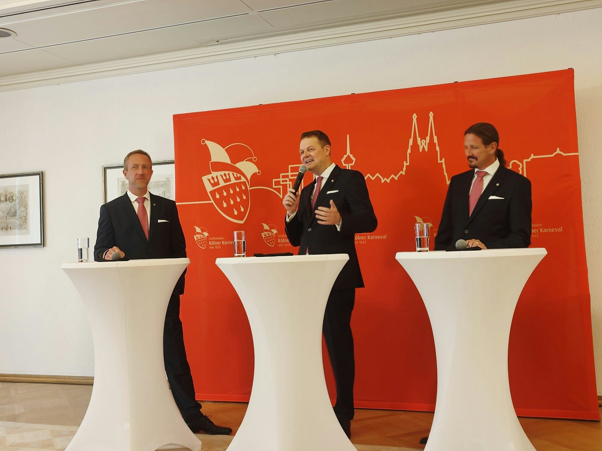 Das neue Kölner Dreigestirn stellt sich am Neumarkt vor. Alle drei stehen an Stehtischen.