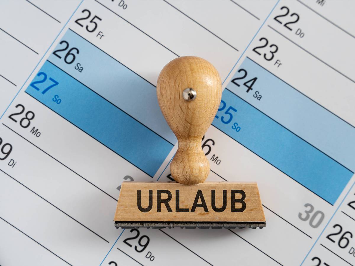 Das Foto ist ein Symbolbild. Es ist ein Kalender zu sehen auf dem ein Stempel mit den Großbuchstaben Urlaub liegt.