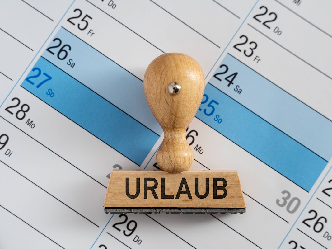 Das Foto ist ein Symbolbild. Es ist ein Kalender zu sehen auf dem ein Stempel mit den Großbuchstaben Urlaub liegt.