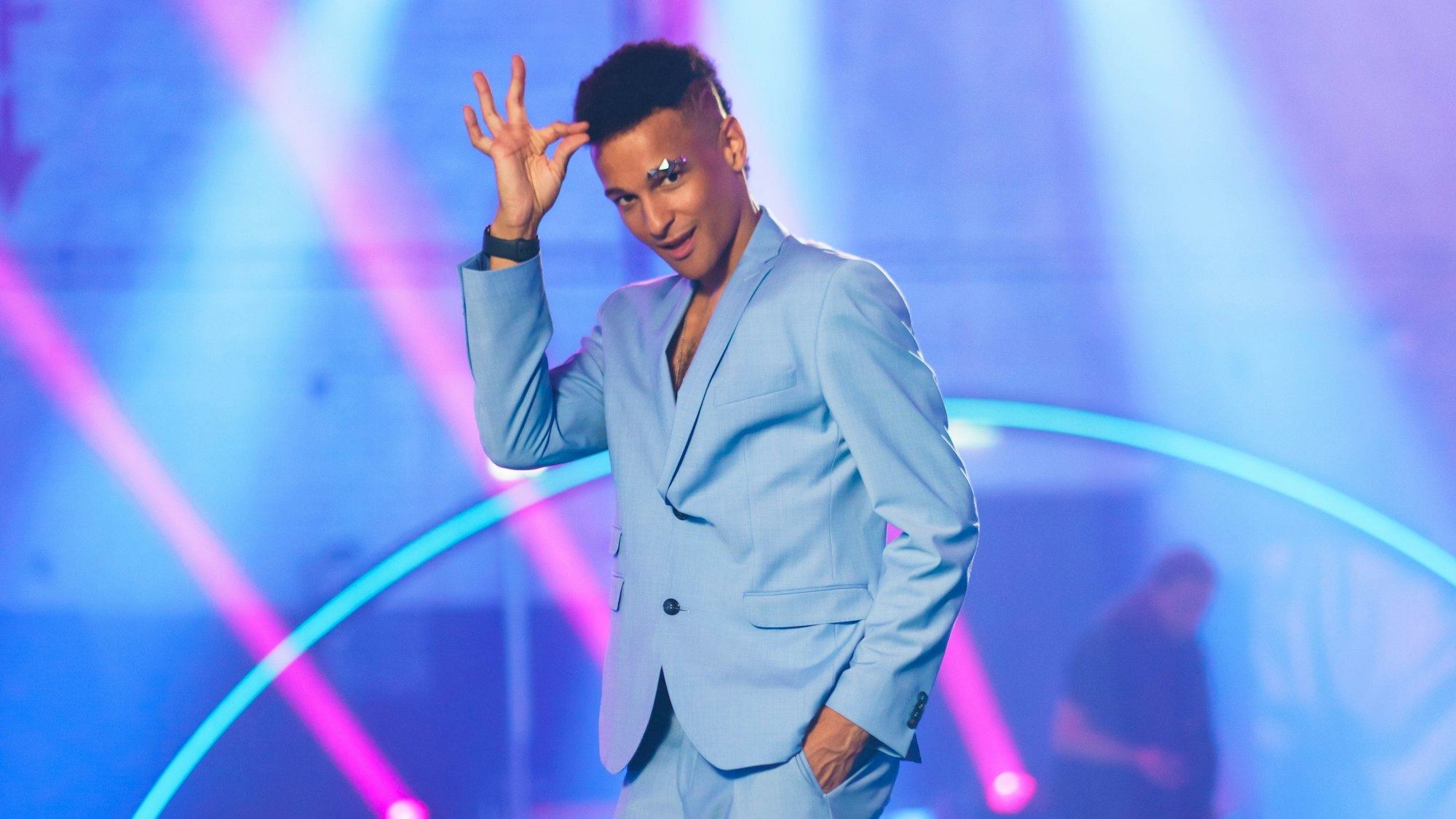 Prince Damien trägt einen blauen Anzug und posiert charmant vor der Kamera.