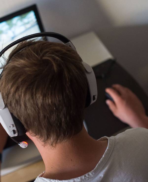 Ein junger Mann sitzt mit einem Headset vor einem Laptop und spielt ein Computerspiel.
