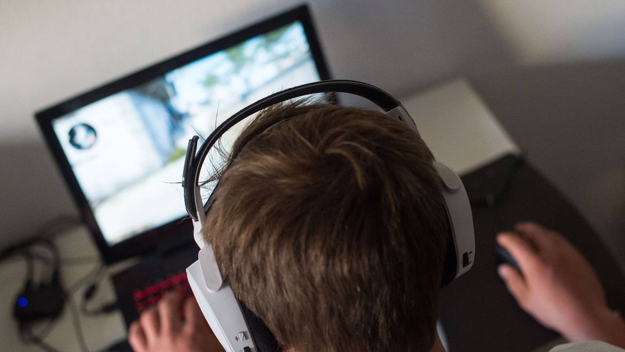 Ein junger Mann sitzt mit einem Headset vor einem Laptop und spielt ein Computerspiel.