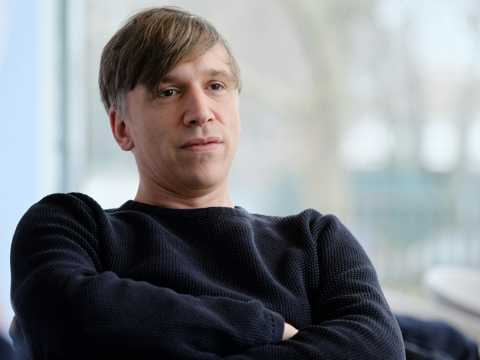 Kasalla-Sänger Bastian Campmann sitzt mit verschränkten Armen bei einem Interview.