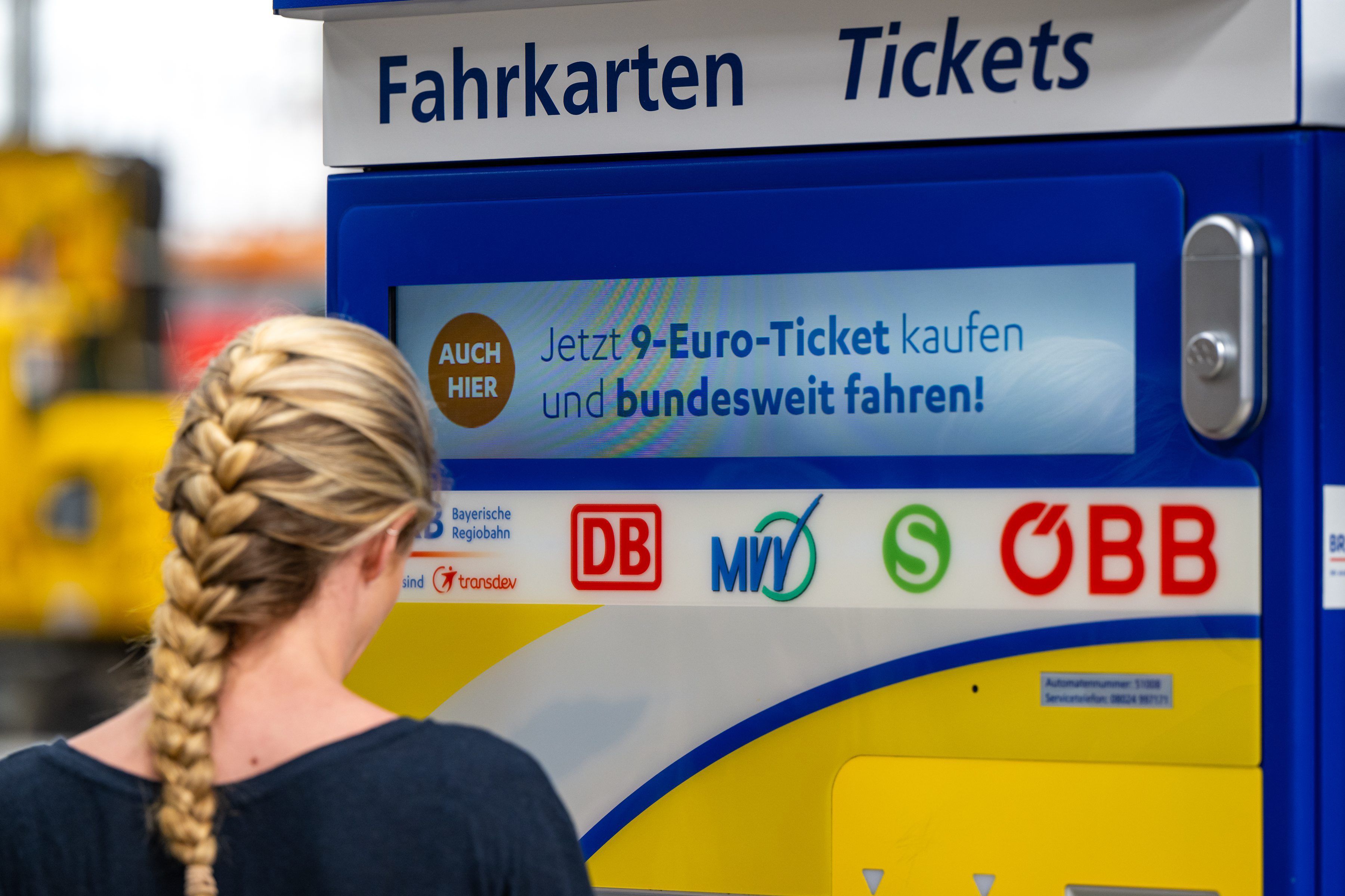 Eine junge Frau steht Anfang Juni 2022 am Münchner Hauptbahnhof an einem Fahrkartenautomaten, auf dem Werbung für das 9-Euro-Ticket zu sehen ist.